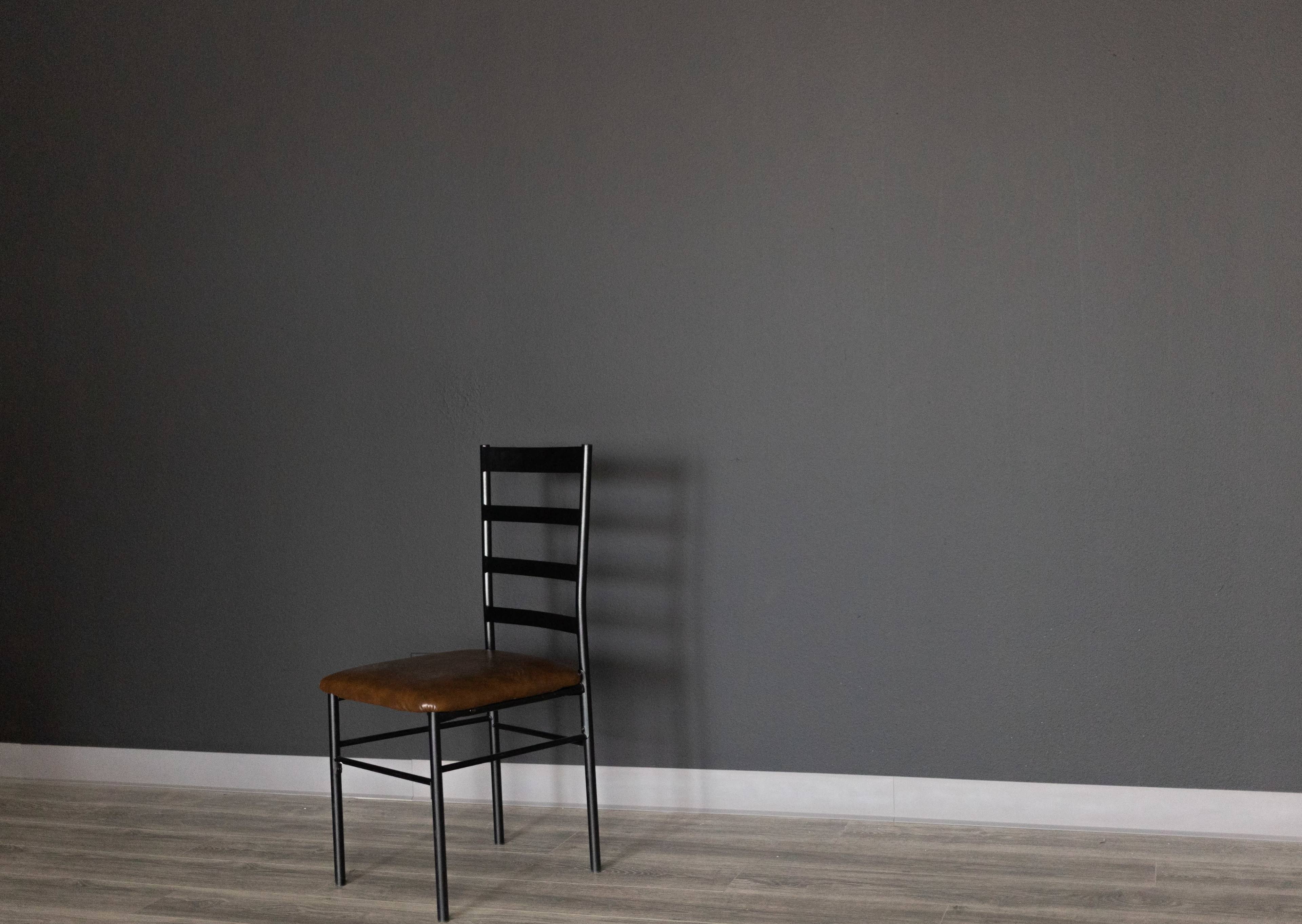 A black metal chair with a brown seat is positioned against a plain gray wall.