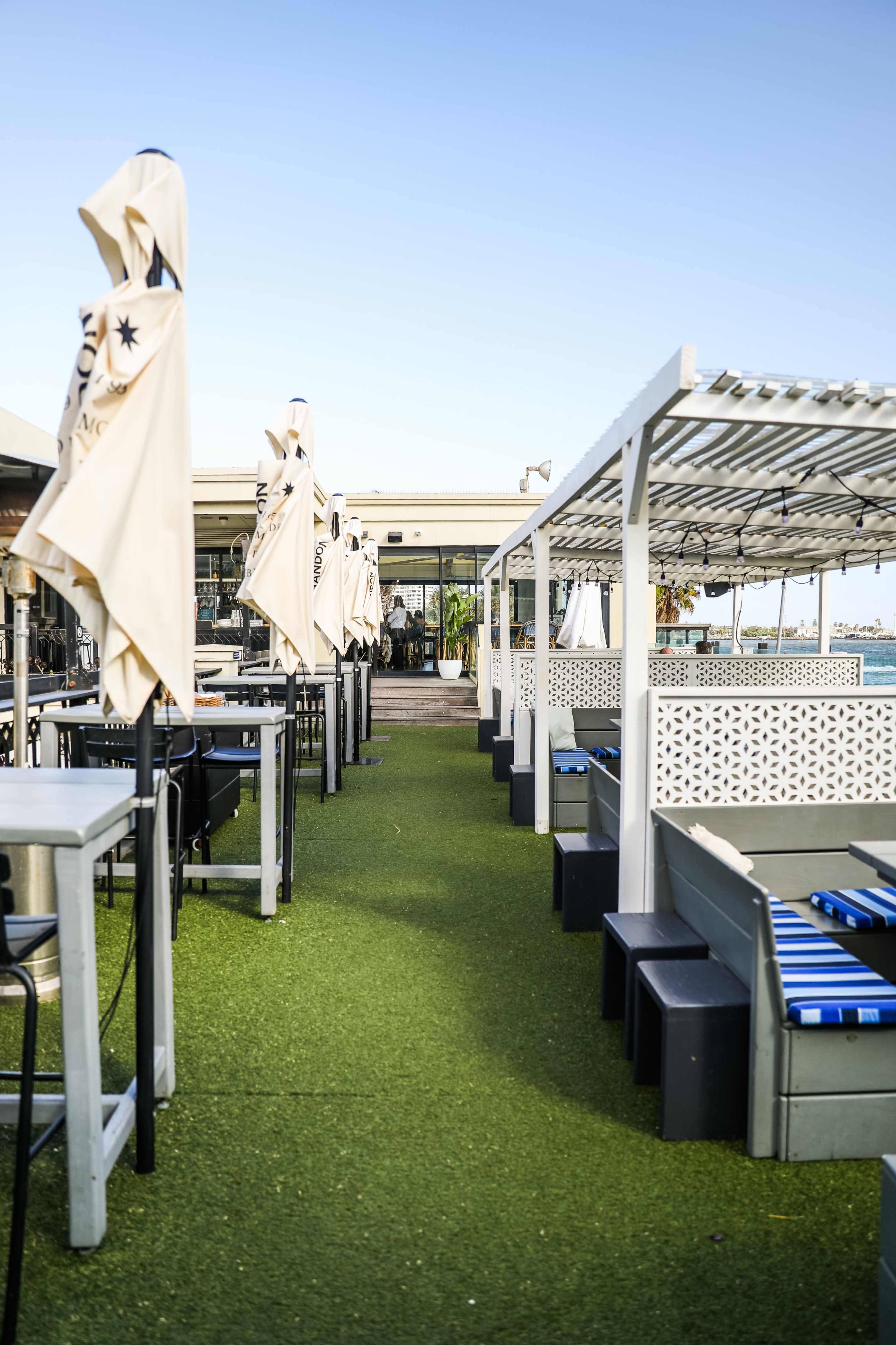 The image shows an outdoor seating area at a restaurant with artificial grass, tables, and umbrellas.