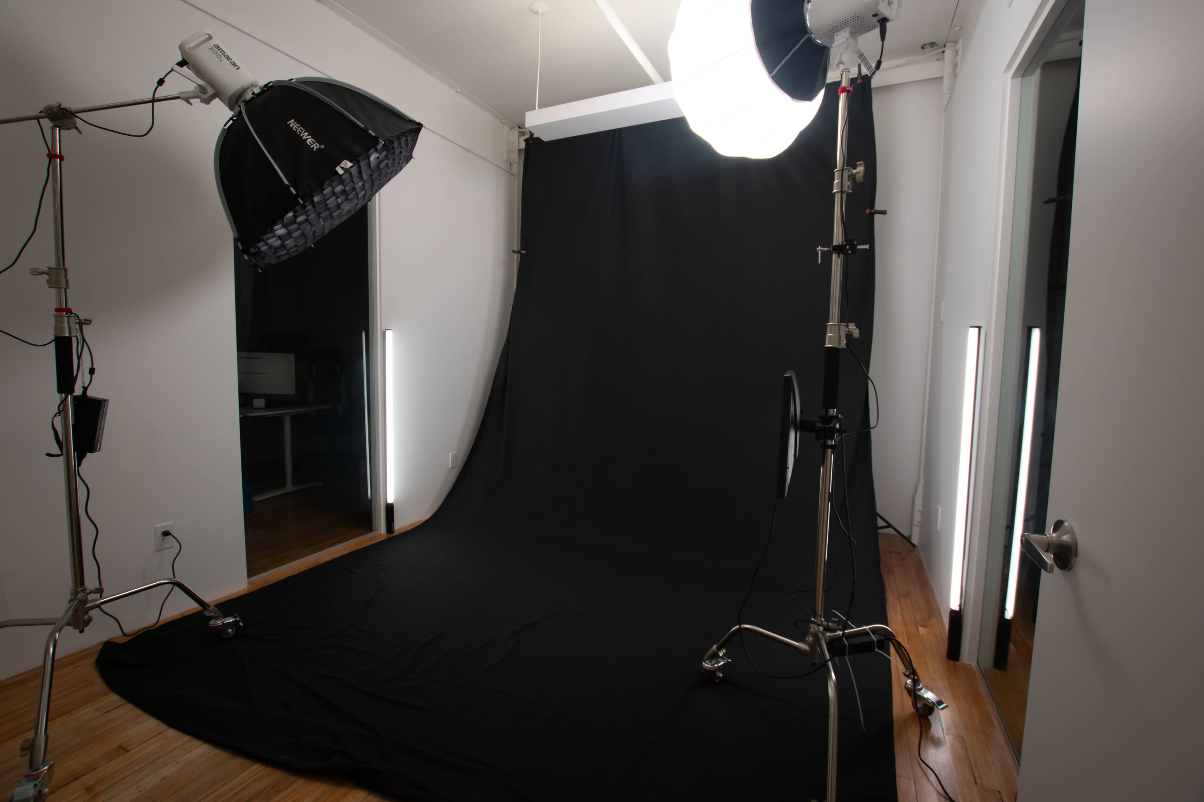 The image shows a photography studio setup with a black backdrop, lighting equipment, and a wooden floor.