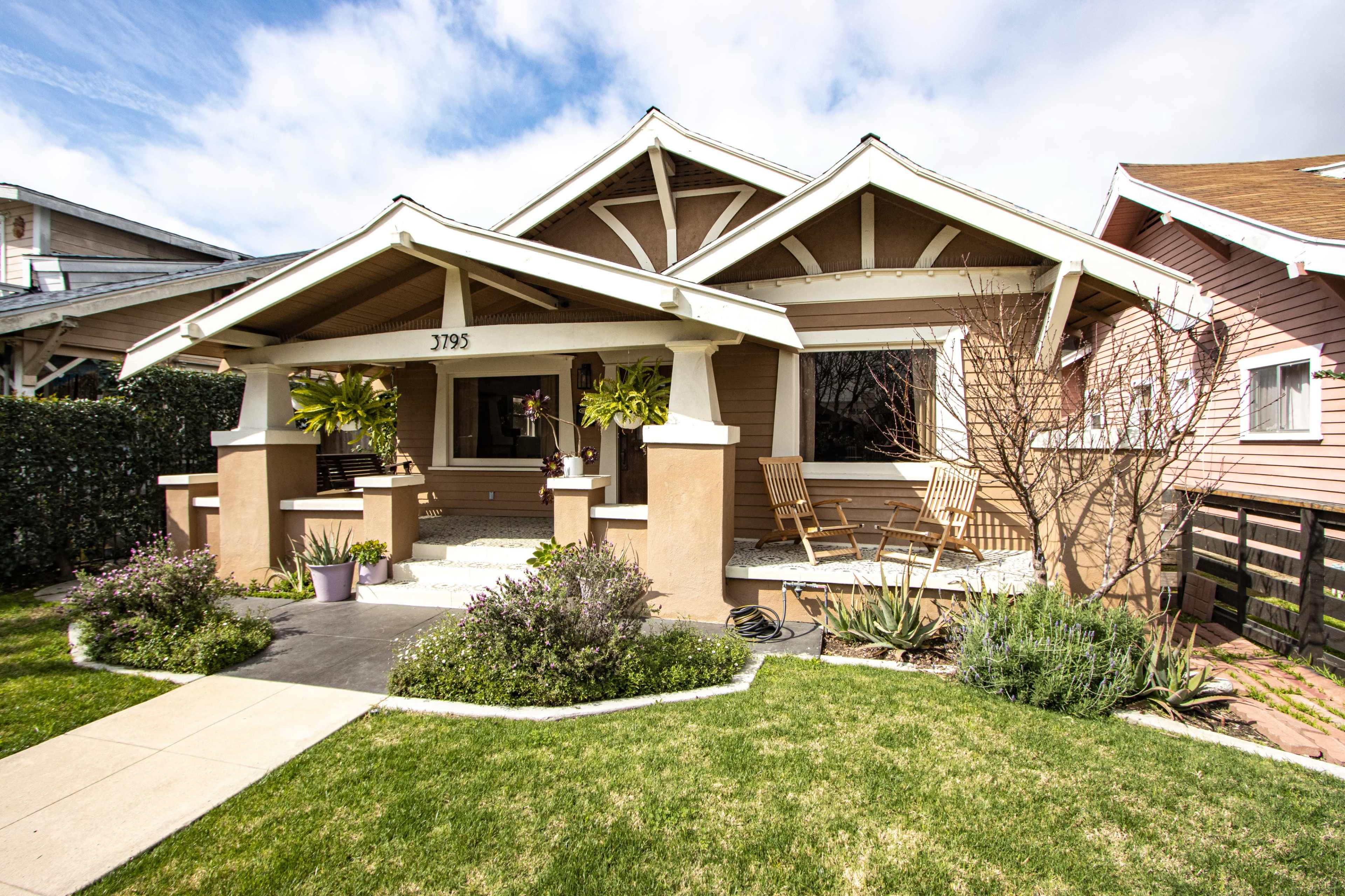 A bungalow-style house with a front porch, surrounded by greenery and a well-maintained lawn.