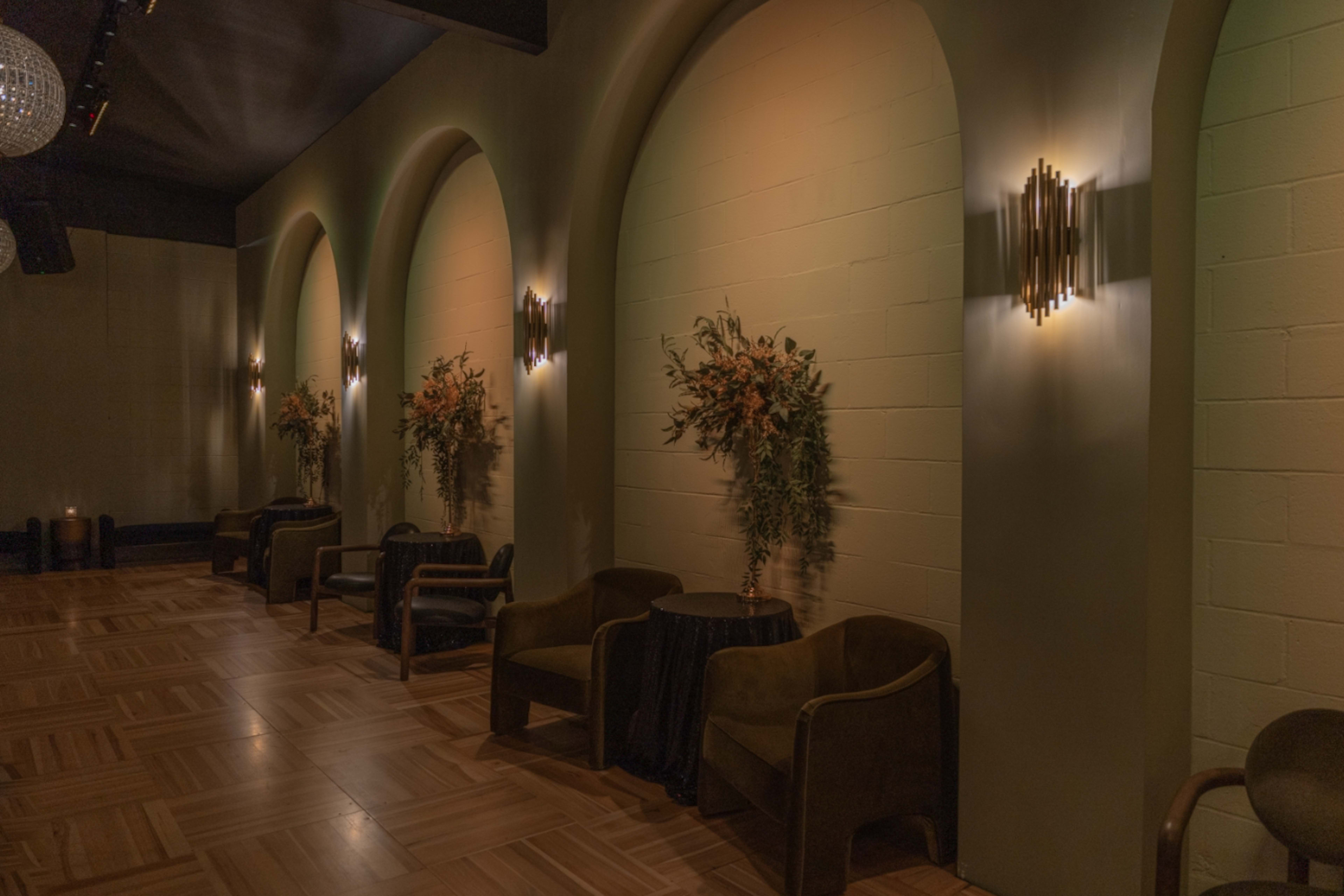 A dimly lit room with green walls featuring archways and decorative plants on either side of two dark seating areas.
