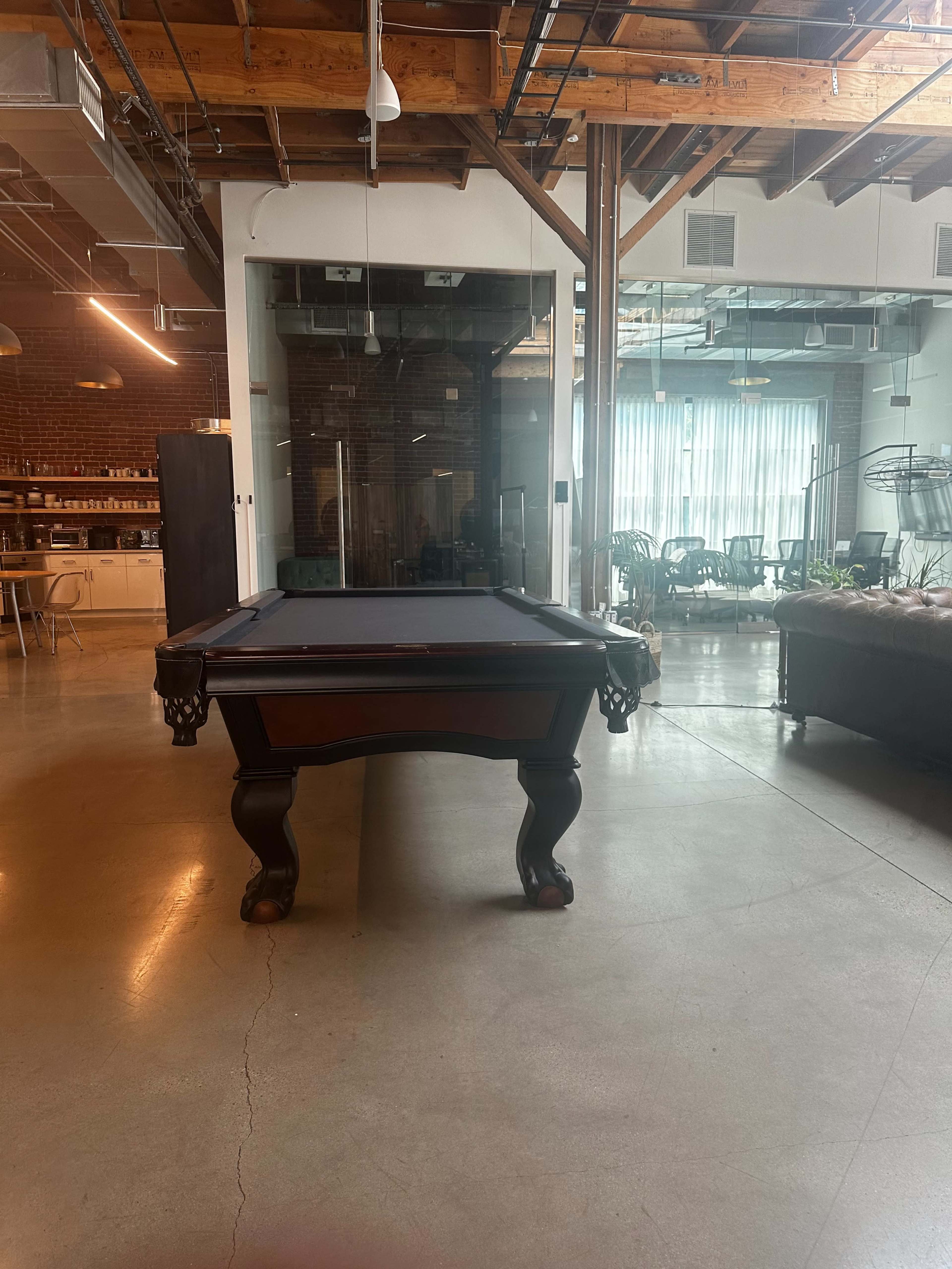 The image shows a billiard table in a spacious, well-lit room with wooden beams and large windows.