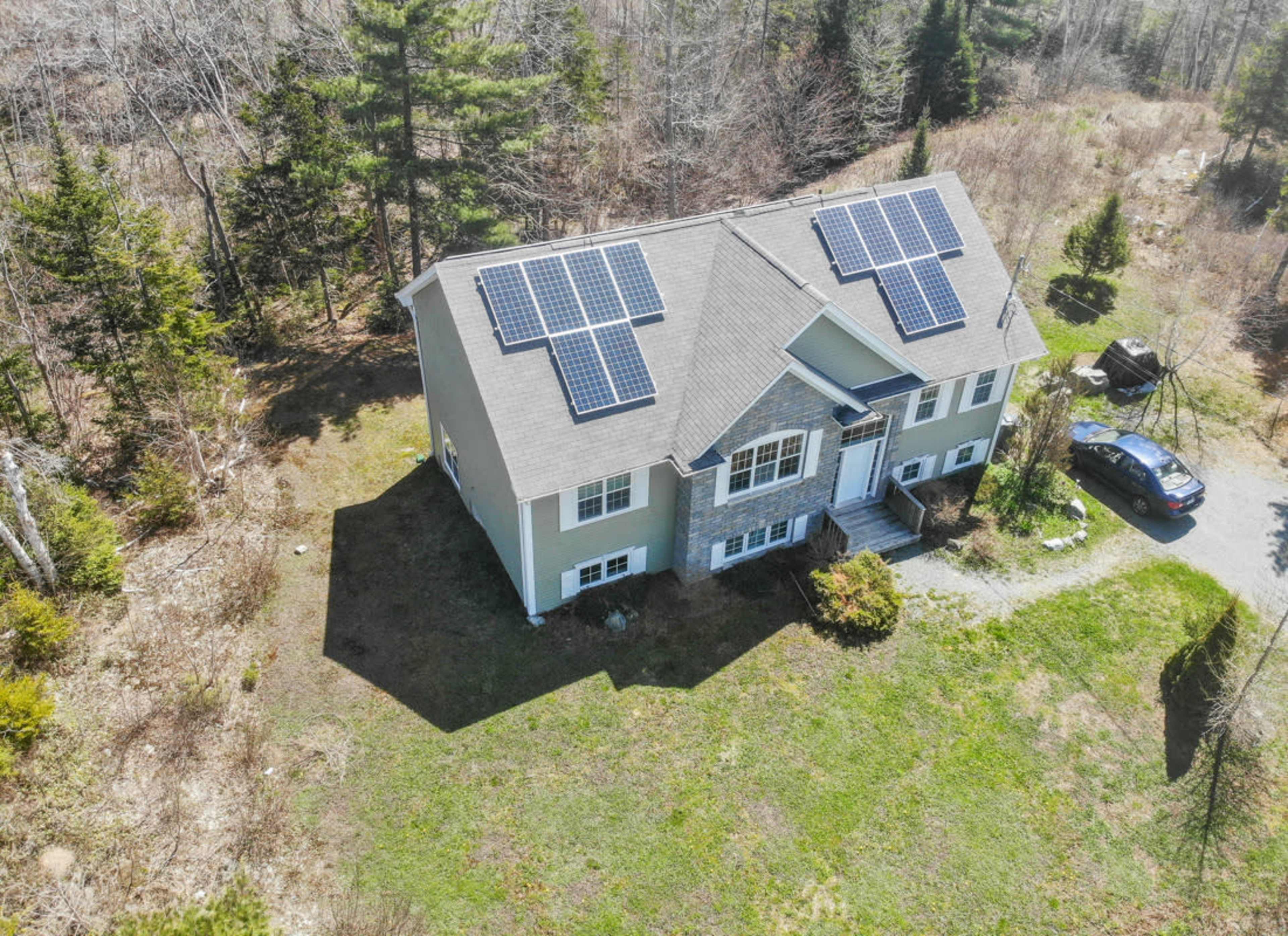 A large house with solar panels on the roof is surrounded by trees and a driveway.
