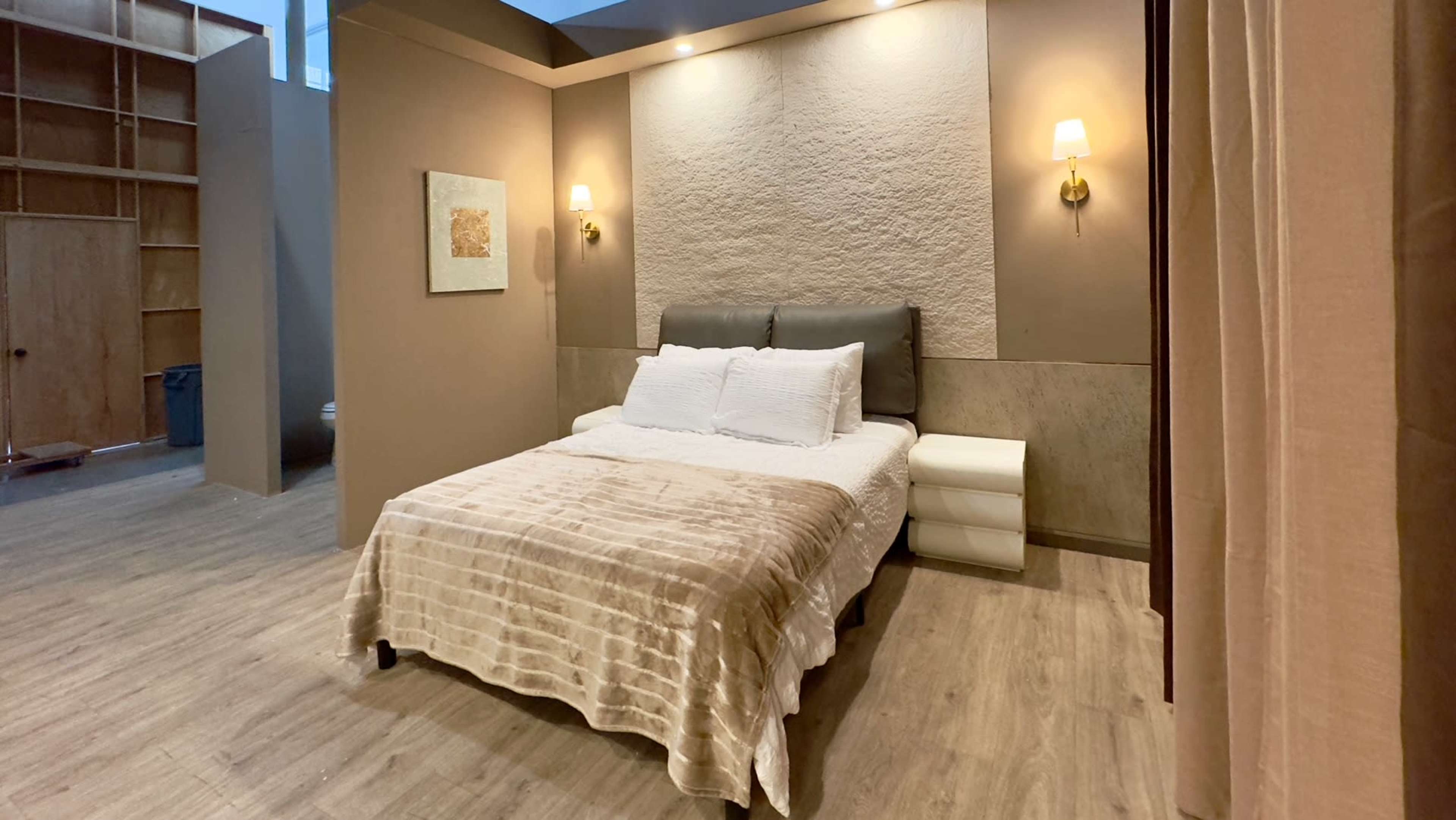 A modern bedroom featuring a bed with a light-colored coverlet, a nightstand, and soft lighting on the walls.