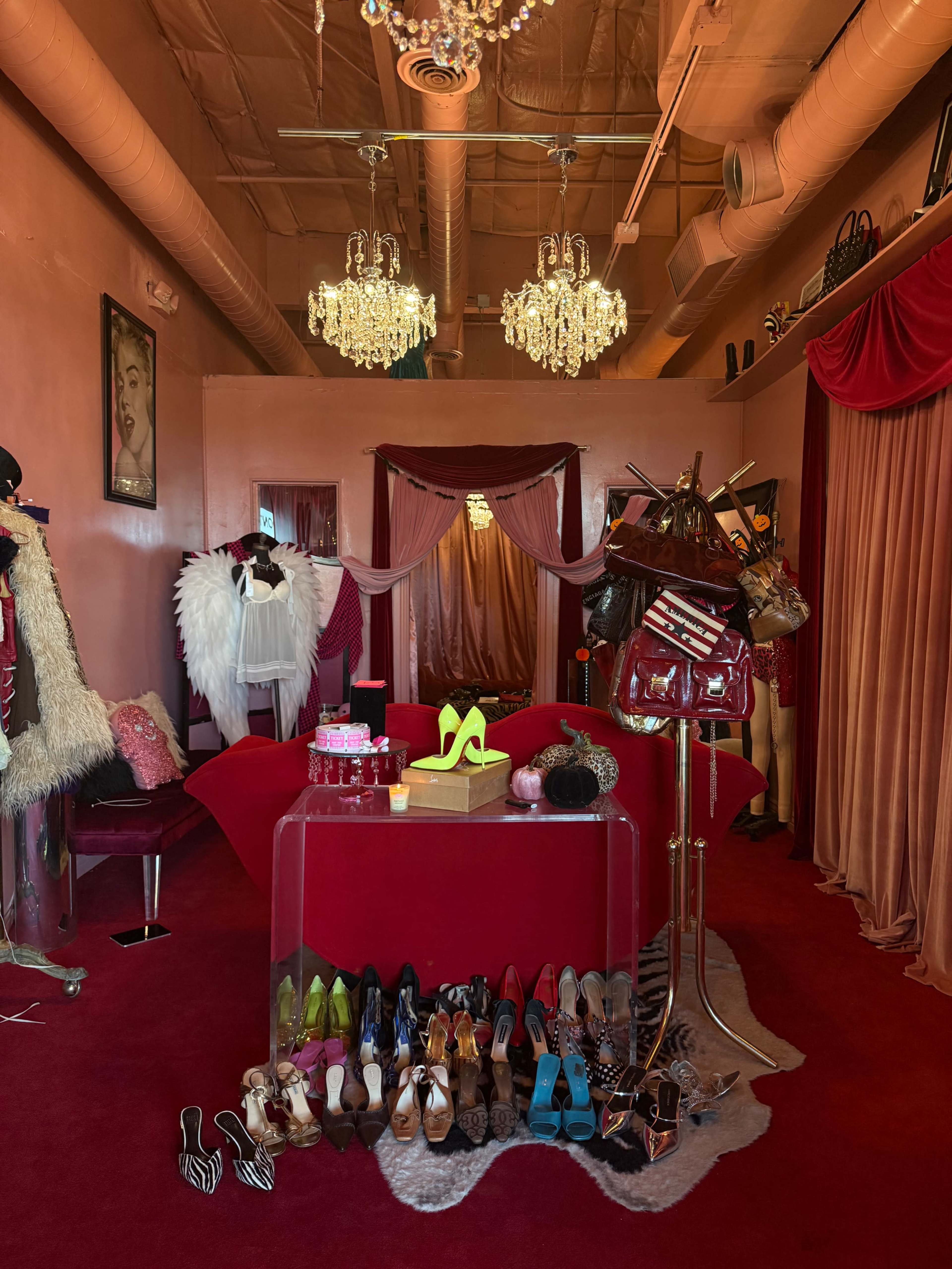 The image shows a fashion boutique with a red and pink color scheme, featuring racks of clothing, a display of high-heeled shoes at the front, and chandeliers hanging from the ceiling.