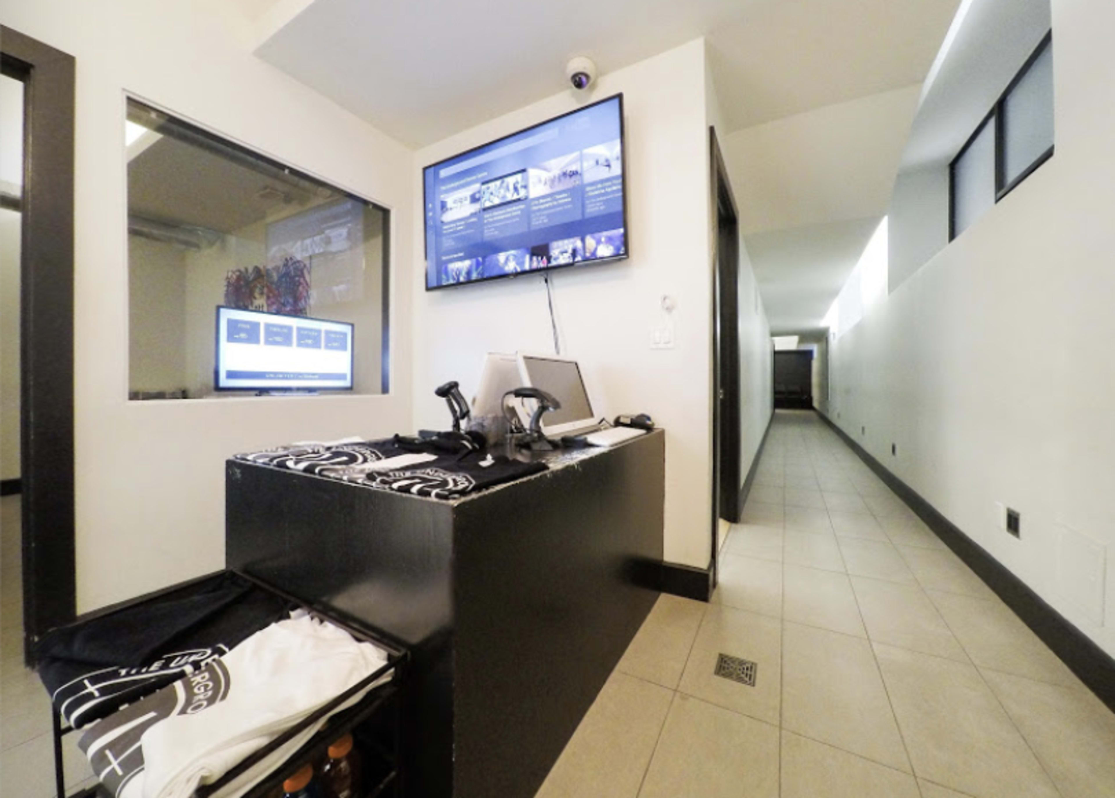 A reception area with a monitor displaying information, a computer setup, and a hallway leading to a darker area.