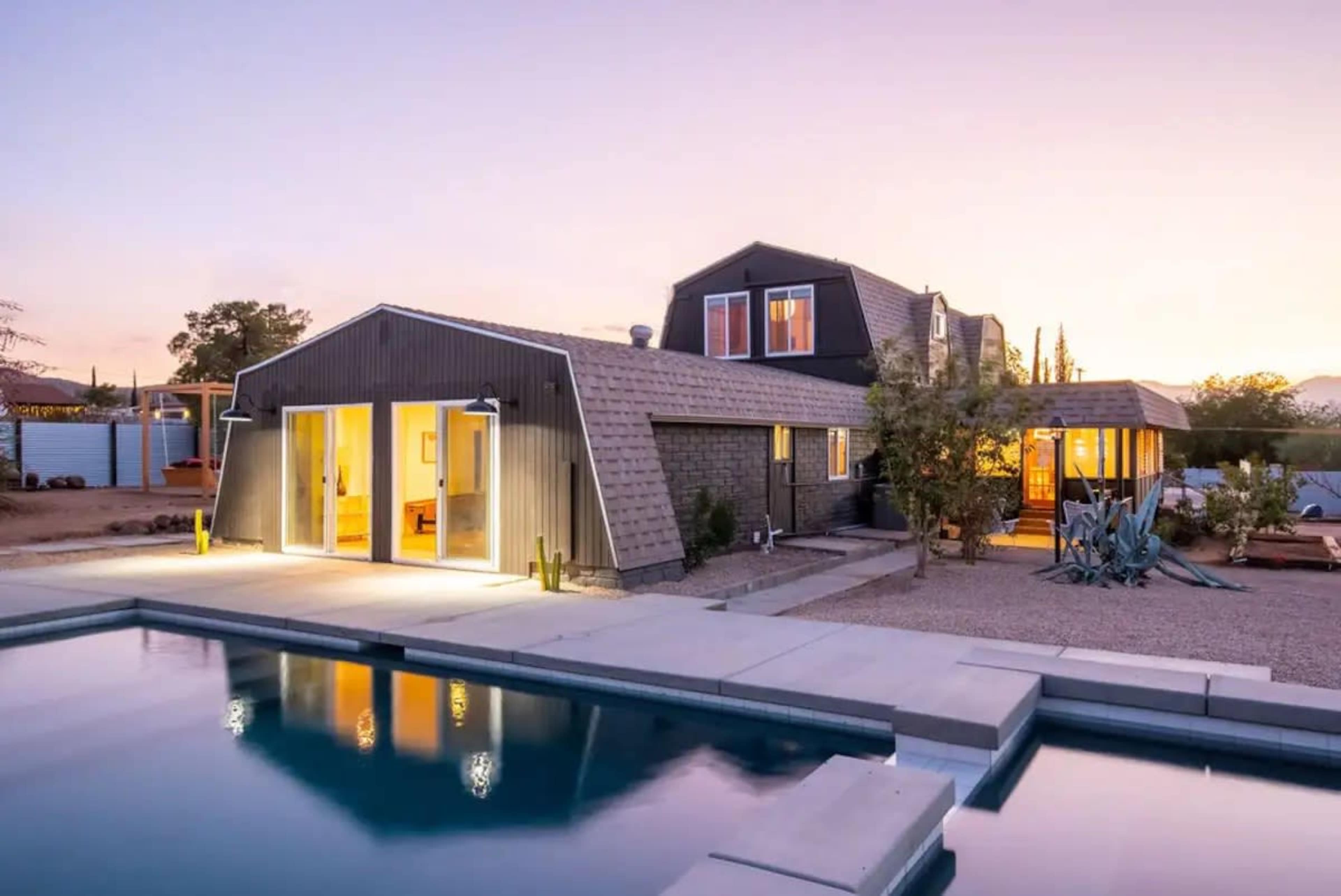A modern house with a sloped roof is situated near a pool, reflecting the twilight sky.