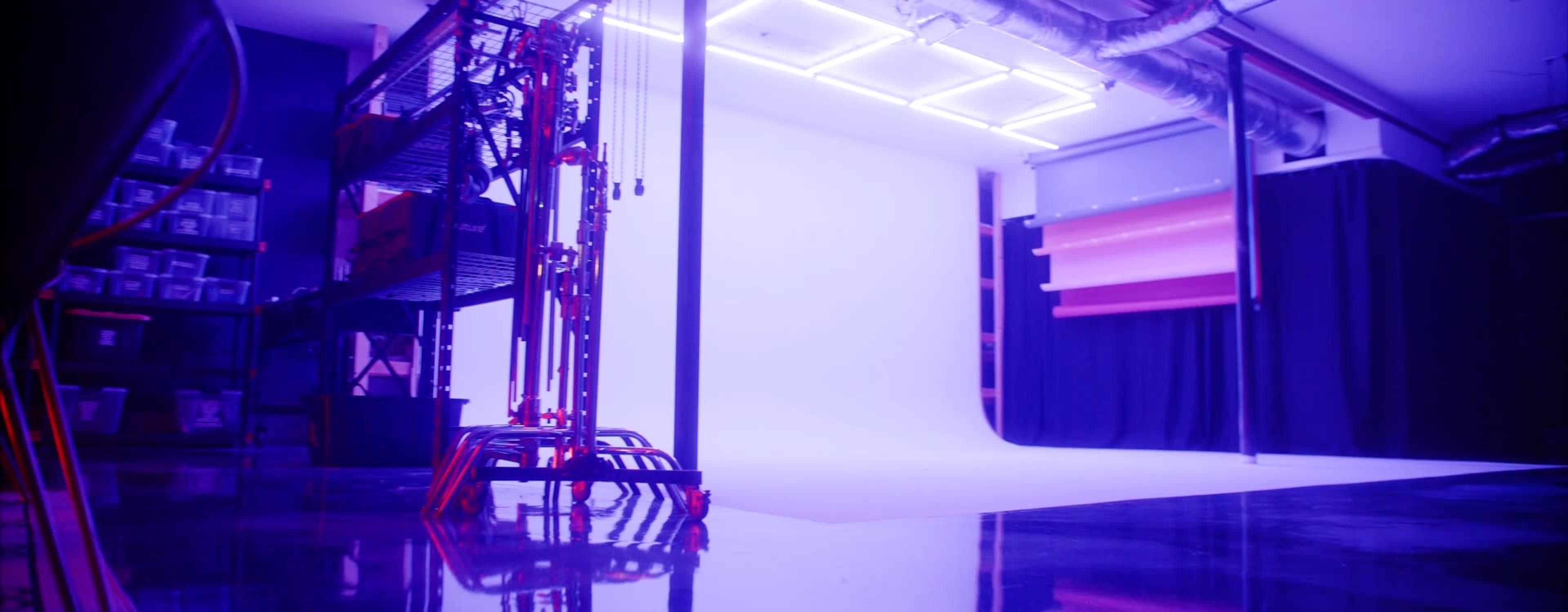 The image shows a well-lit photography studio with purple and white lighting and a seamless backdrop.