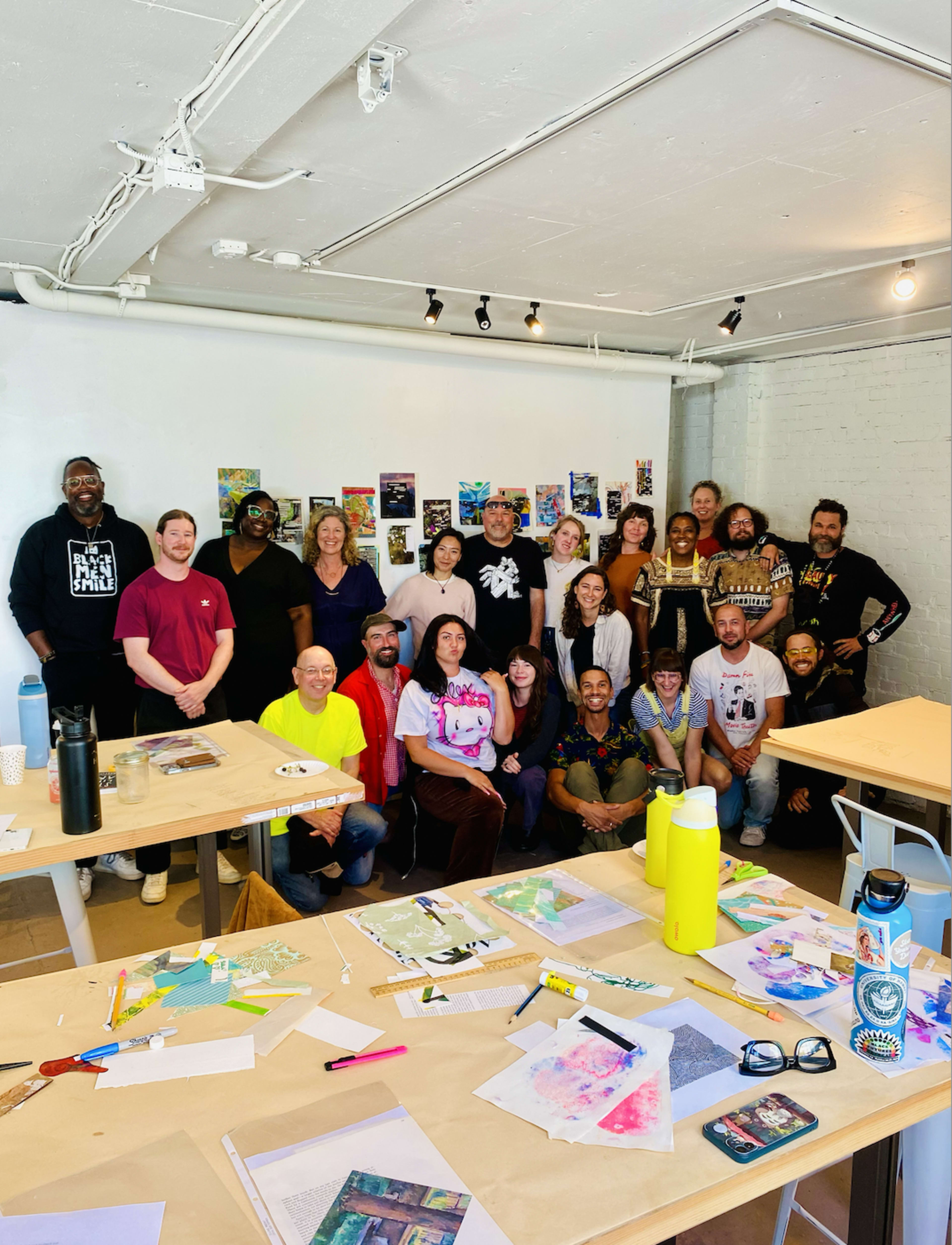 A diverse group of individuals poses together in a studio setting, surrounded by art supplies and colorful artwork displayed on the walls.