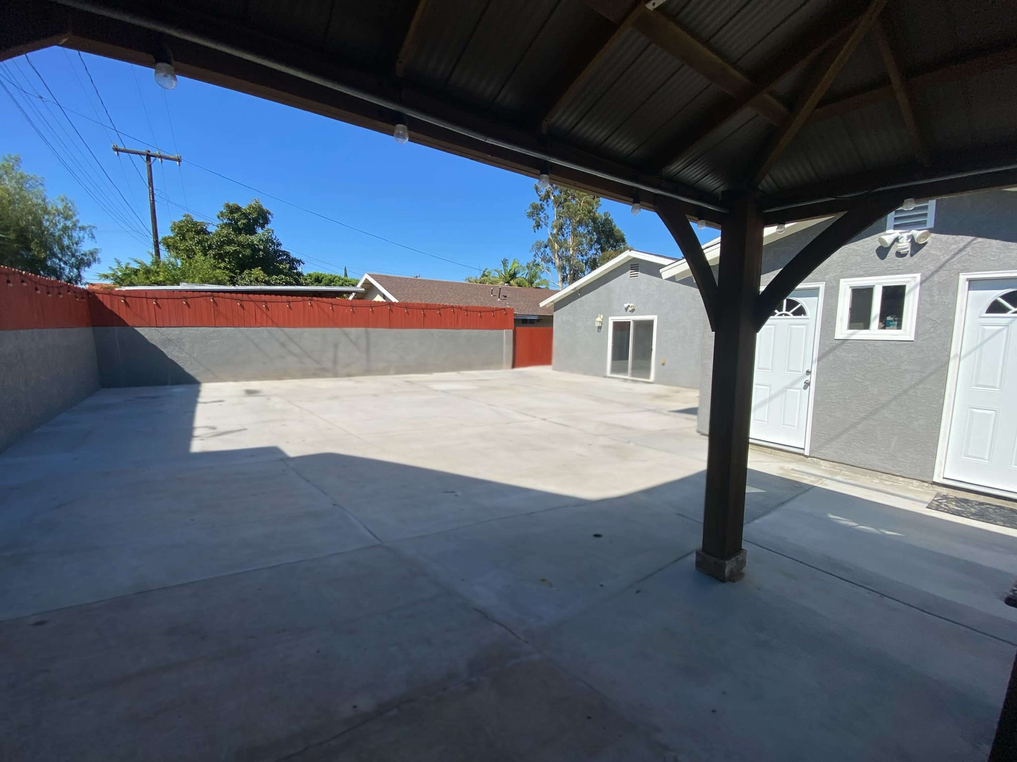 The image shows a large, empty outdoor concrete area enclosed by walls and featuring a covered structure with wooden beams.