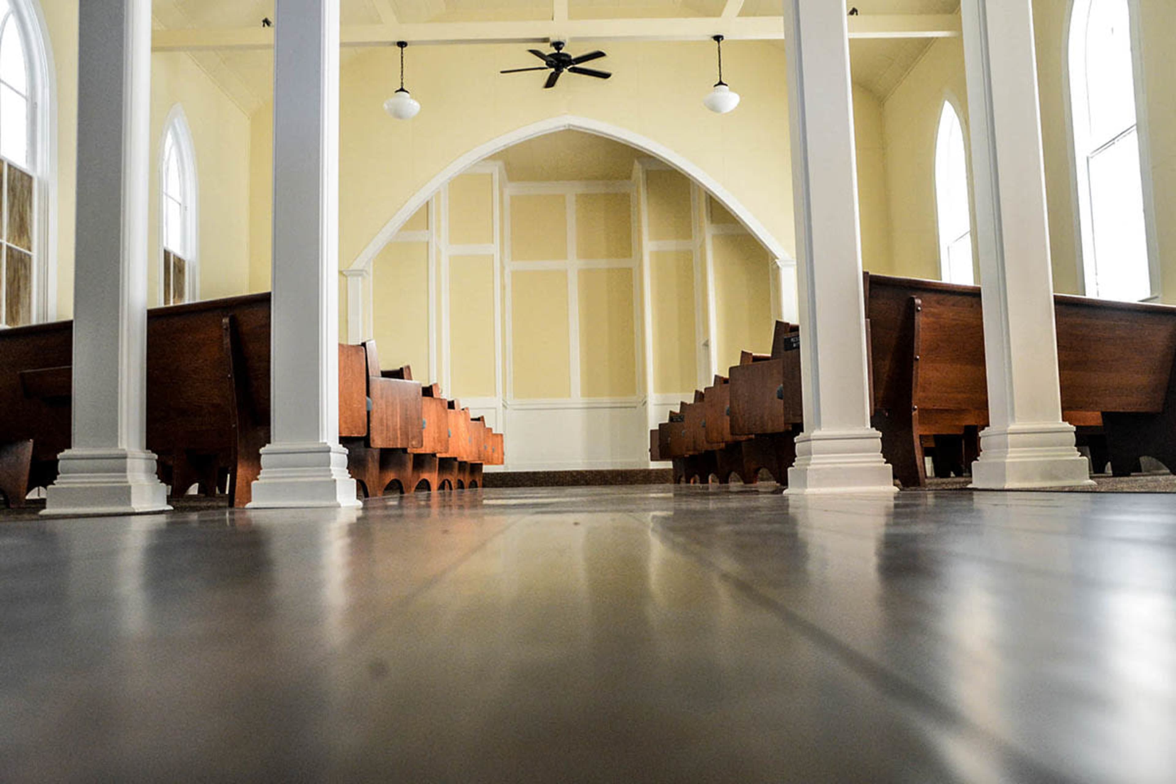 The interior of a church with wooden pews arranged in rows along a polished floor under tall, white columns.