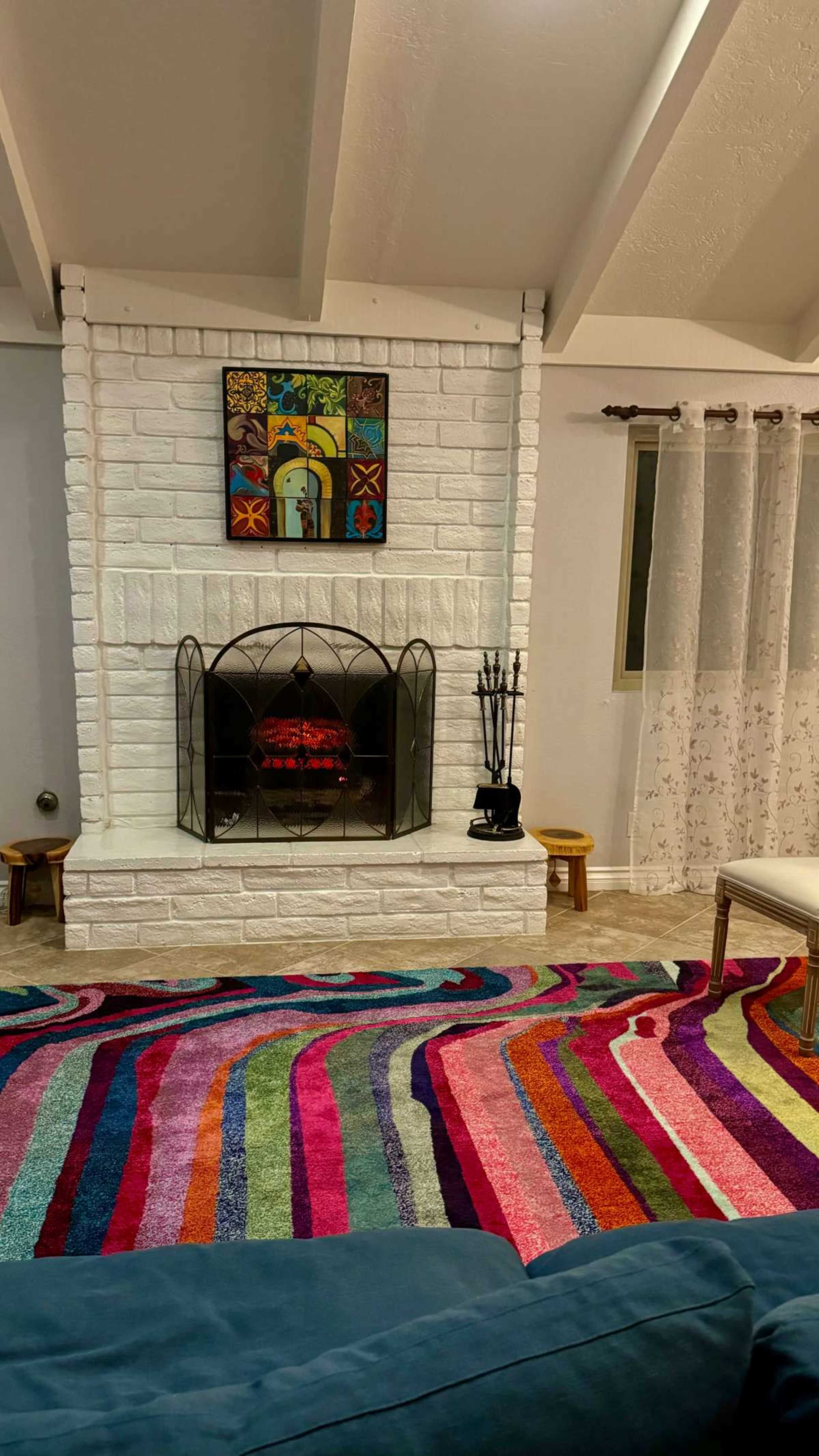 The image shows a living room with a white-brick fireplace, colorful rug, and decorative wall art above the mantle.