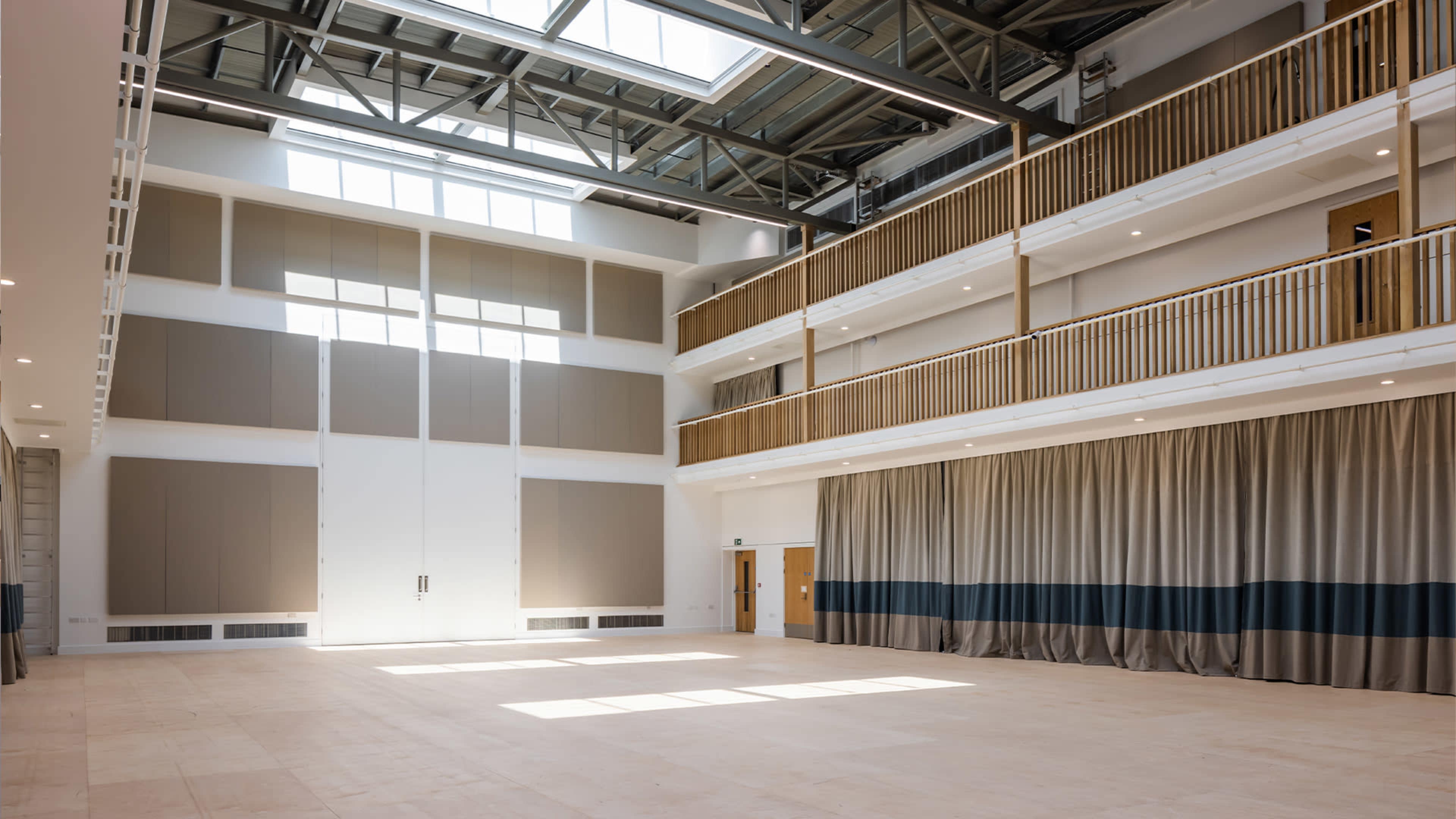 A spacious interior area with high ceilings, large windows, and a stage area draped with curtains.