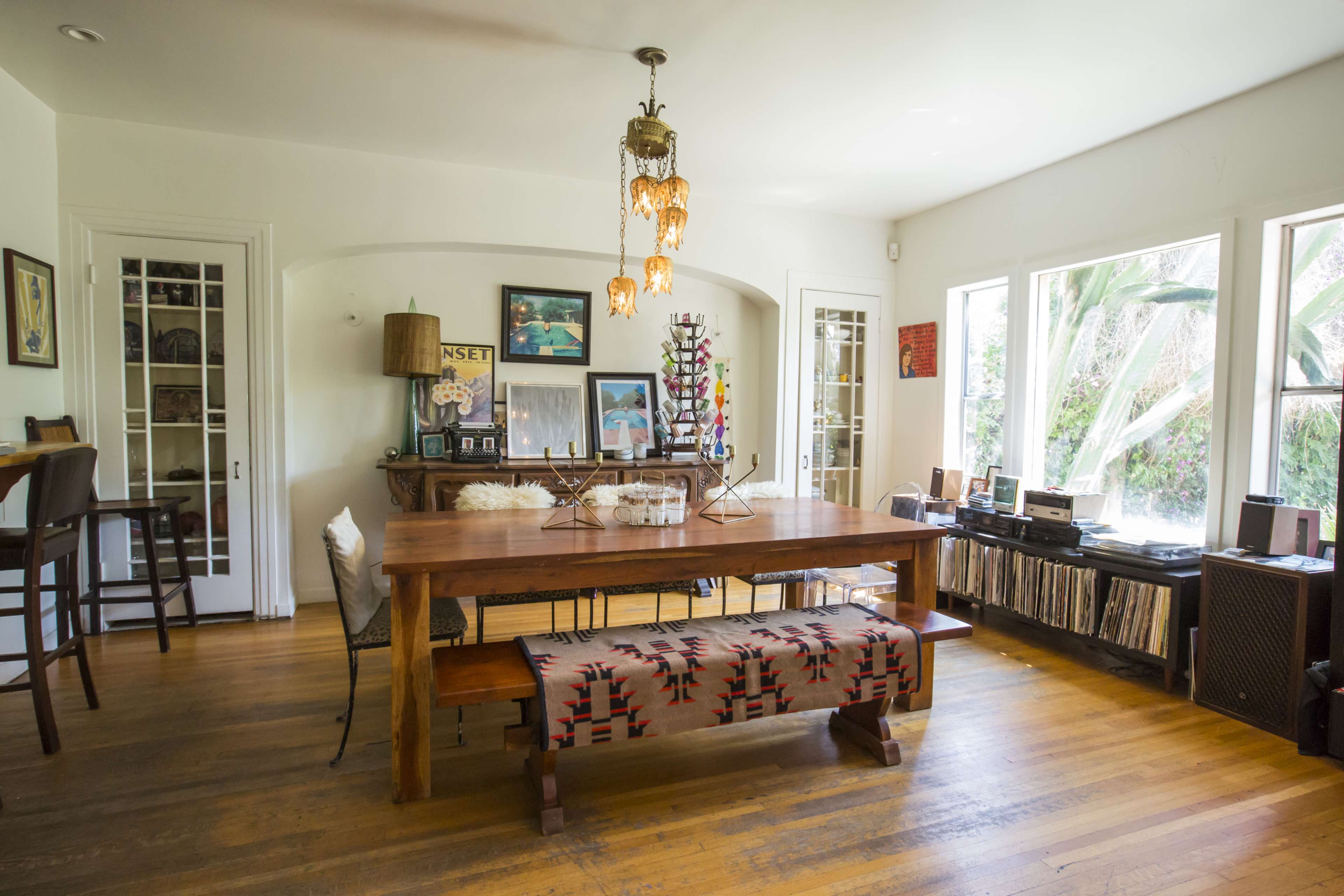 A bright dining room with a wooden table, a long bench, and a collection of framed artwork and records on display.
