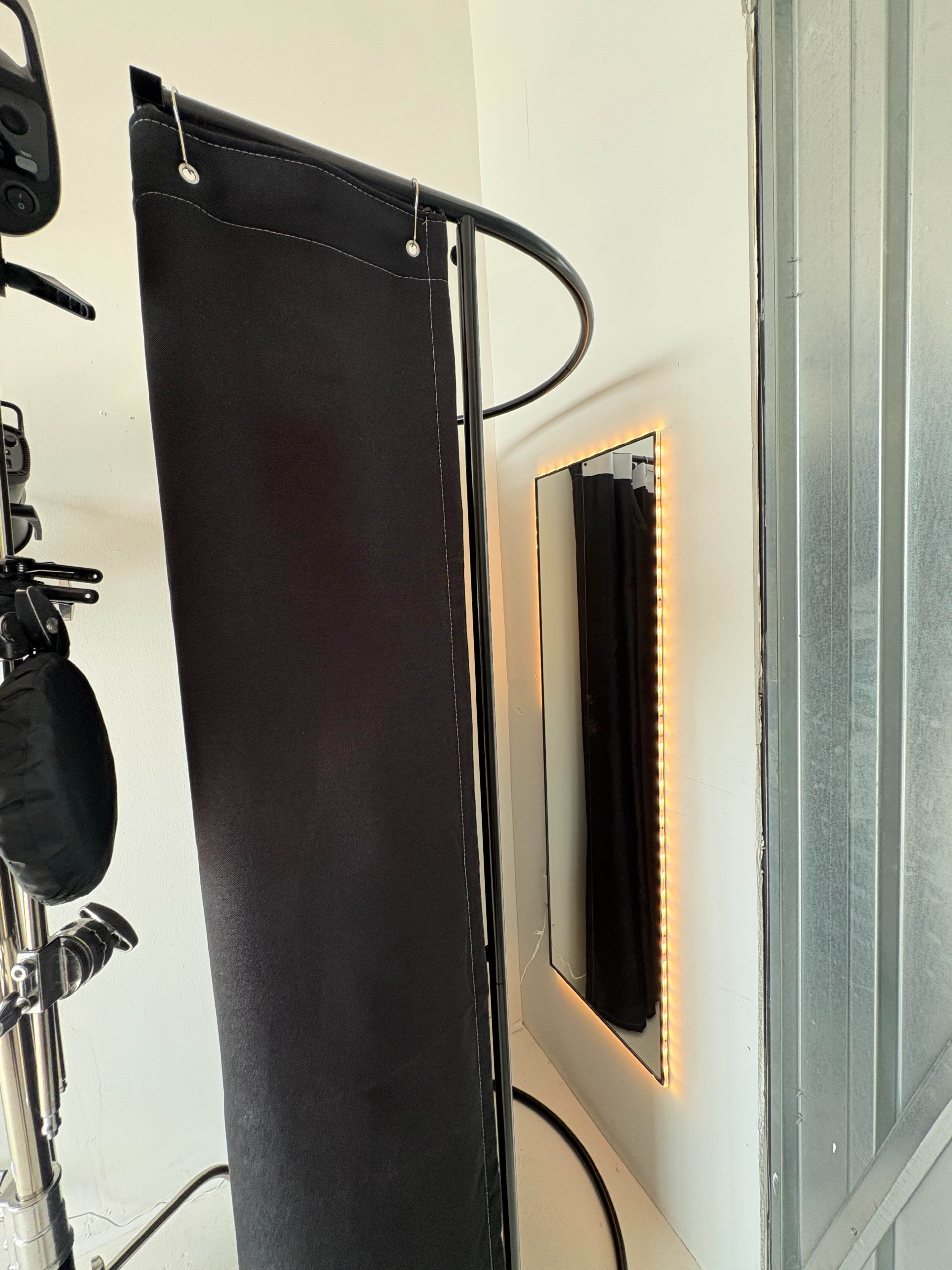 The image shows a black curtain hanging on a rod beside a backlit mirror in a well-lit corner of a room.