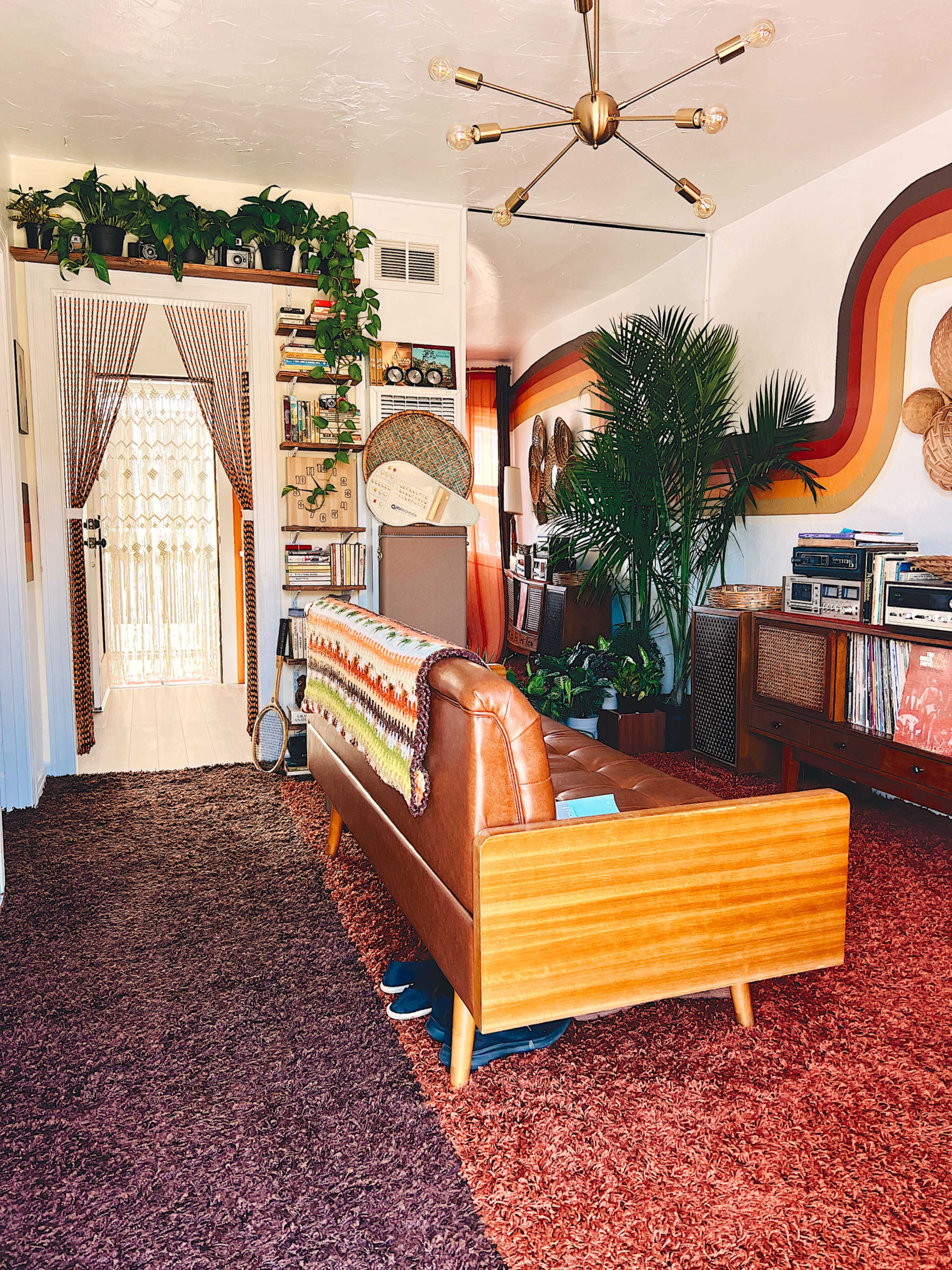 A mid-century modern living room features a wooden sofa with a colorful blanket, plants adorning the walls and shelves, and a record player setup beside a collection of vinyl records.