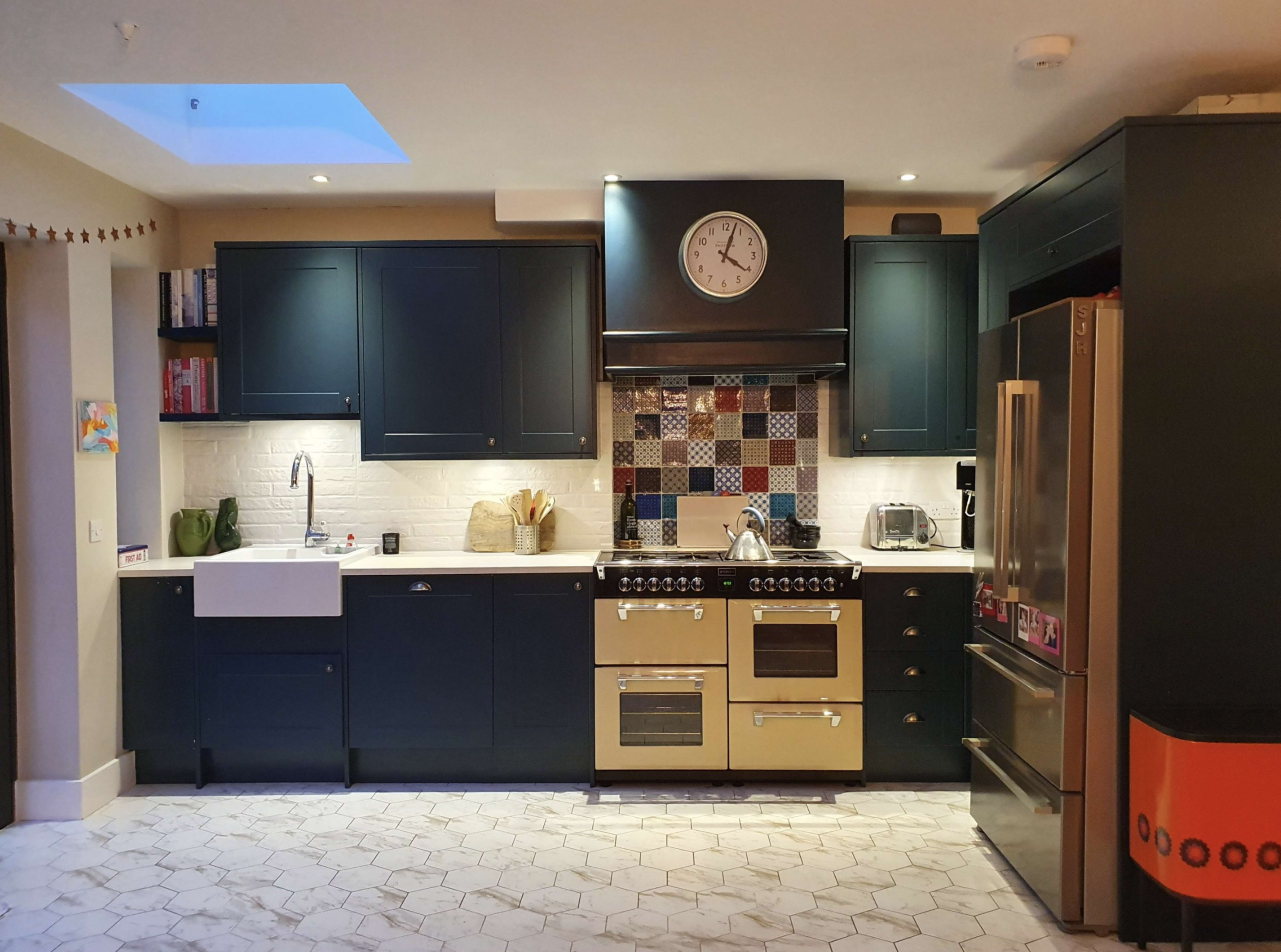 A modern kitchen features dark blue cabinetry, a cream-colored range, and a mosaic tile backsplash, with a farmhouse sink and stainless steel appliances.