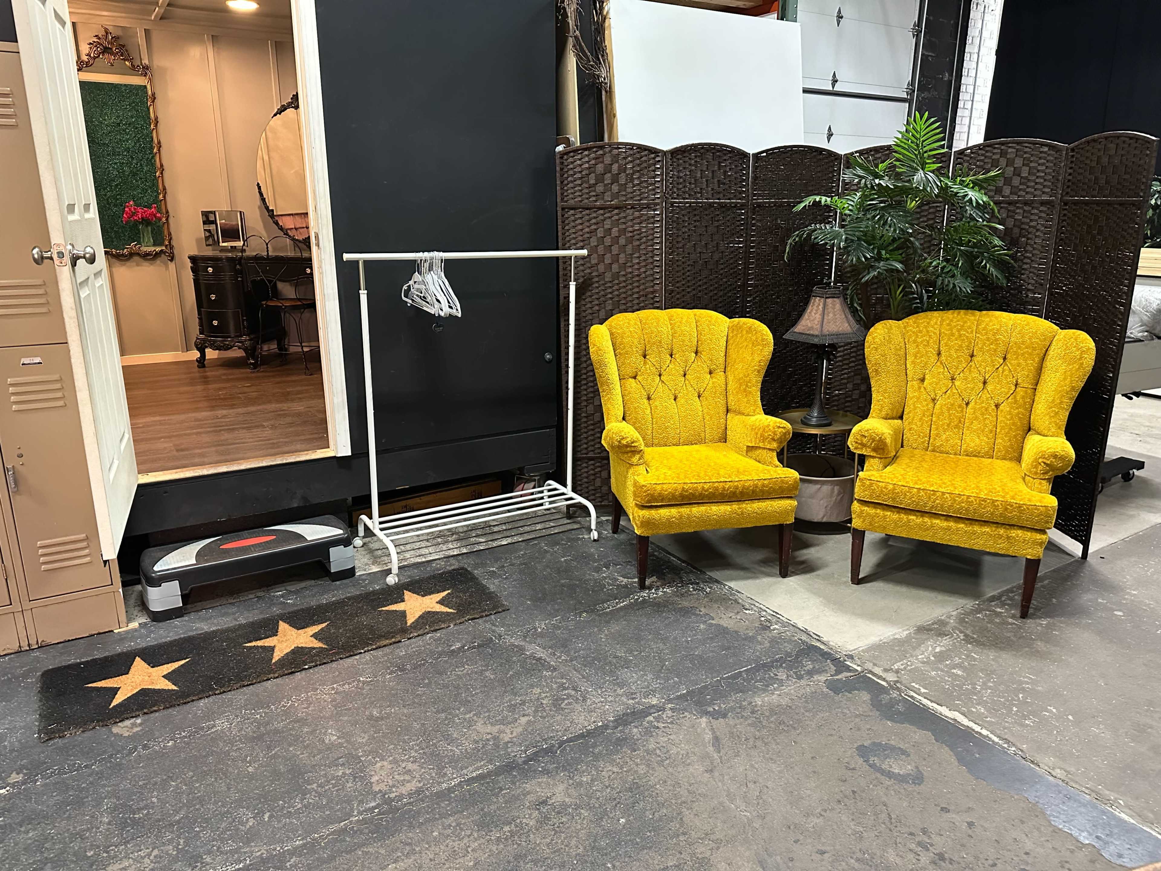 The scene features a pair of yellow armchairs positioned near a white clothing rack and a decorative screen, with a doorway leading to another room in the background.