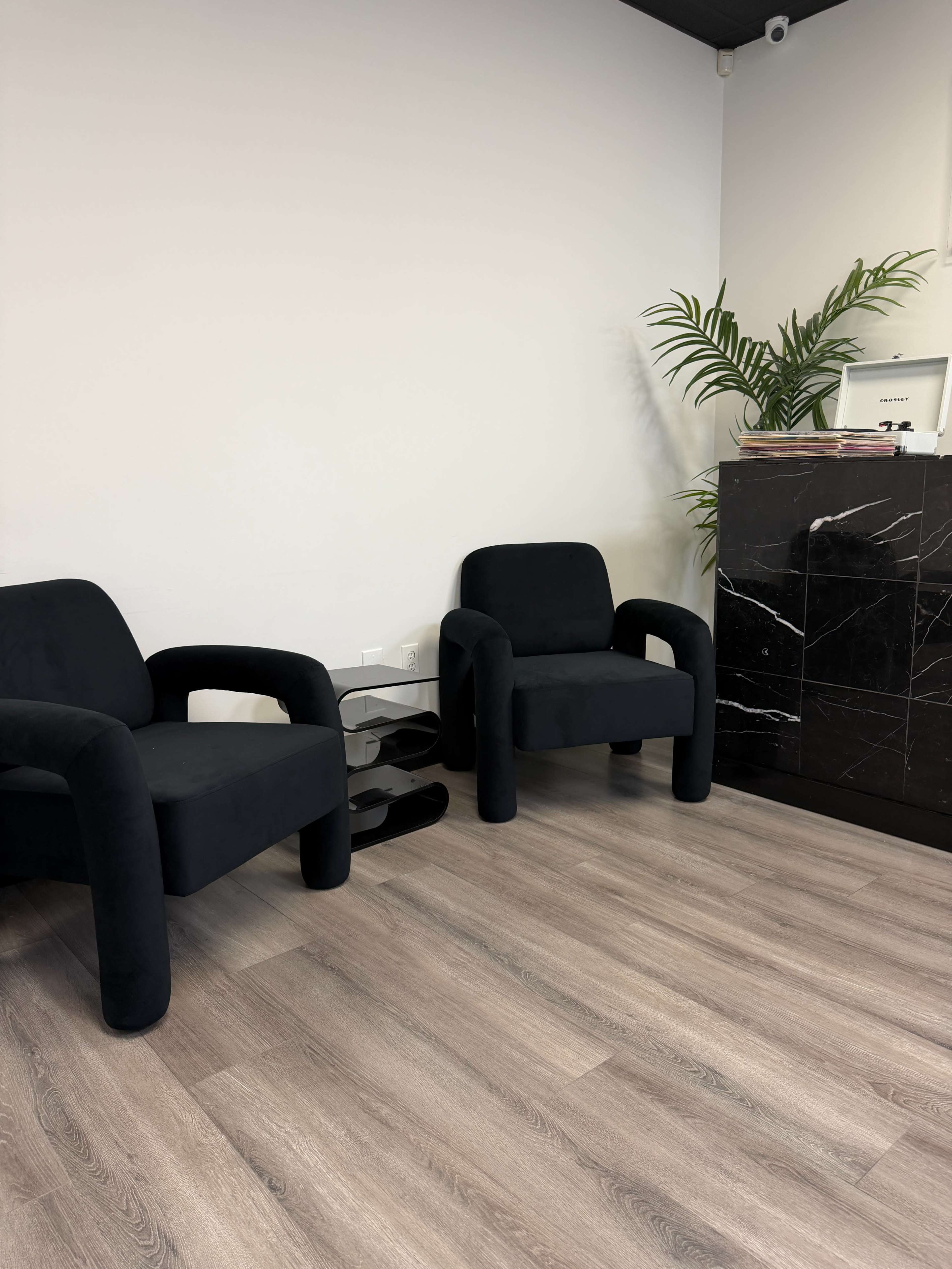 The image shows two black upholstered chairs facing each other in a room with light wooden flooring and a marble reception desk.