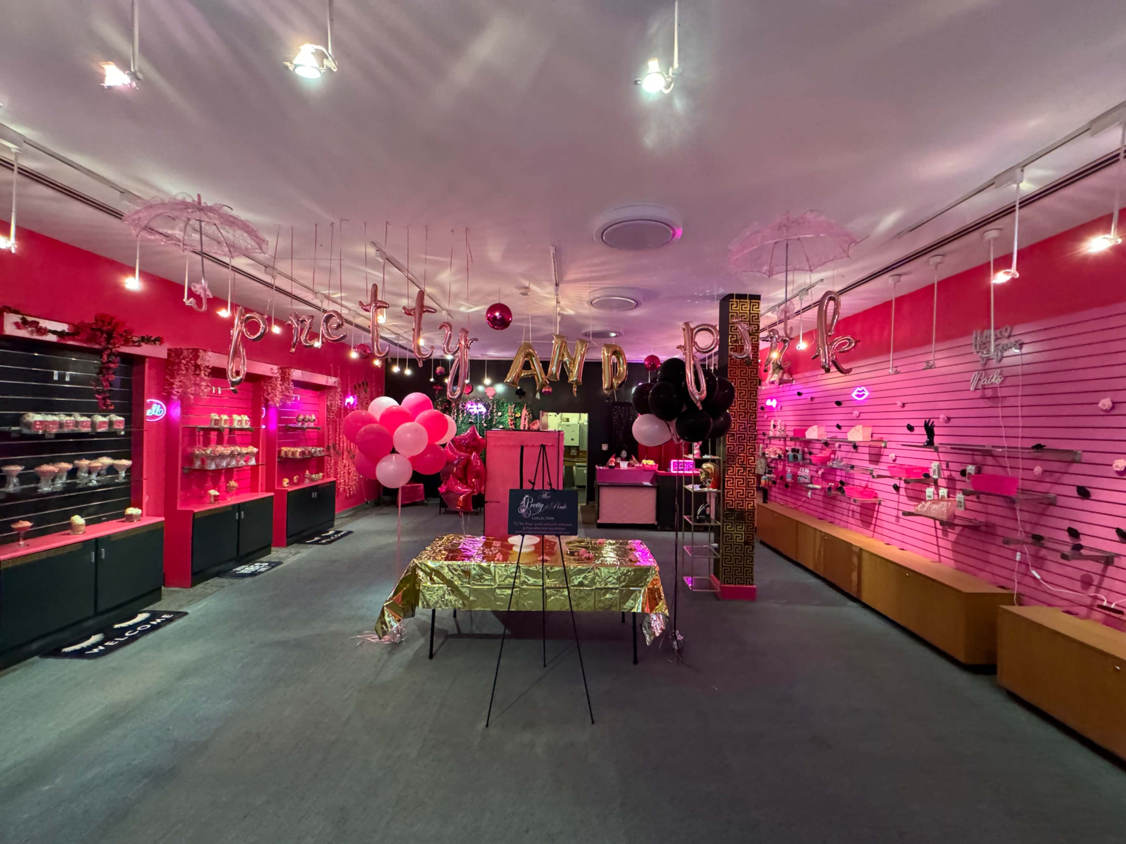 A brightly-colored retail store interior decorated with pink walls, balloons, and various accessories displayed on shelves.
