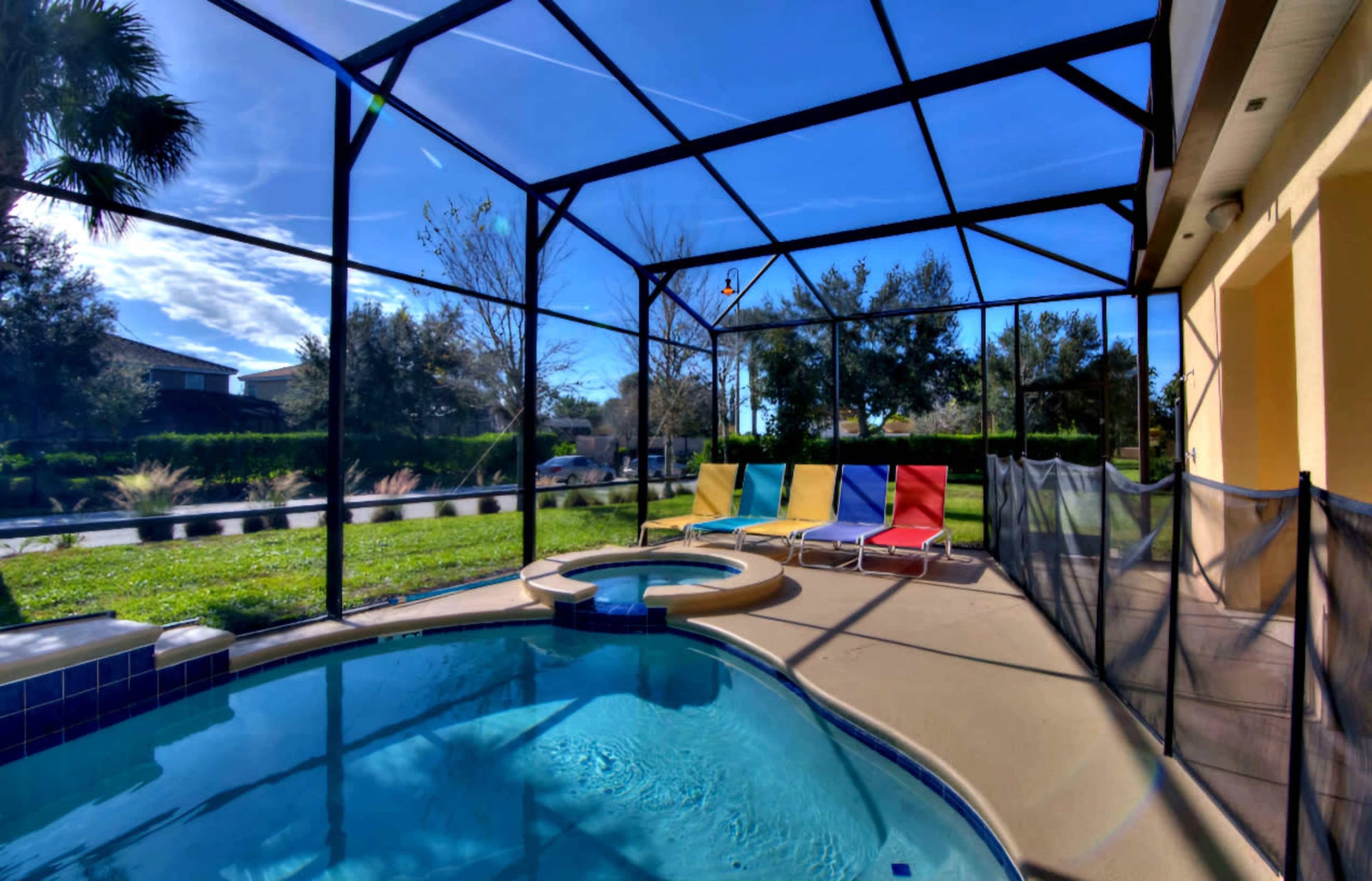 The image depicts a screened-in pool area featuring a circular hot tub, colorful lounge chairs, and a clear blue sky in the background.