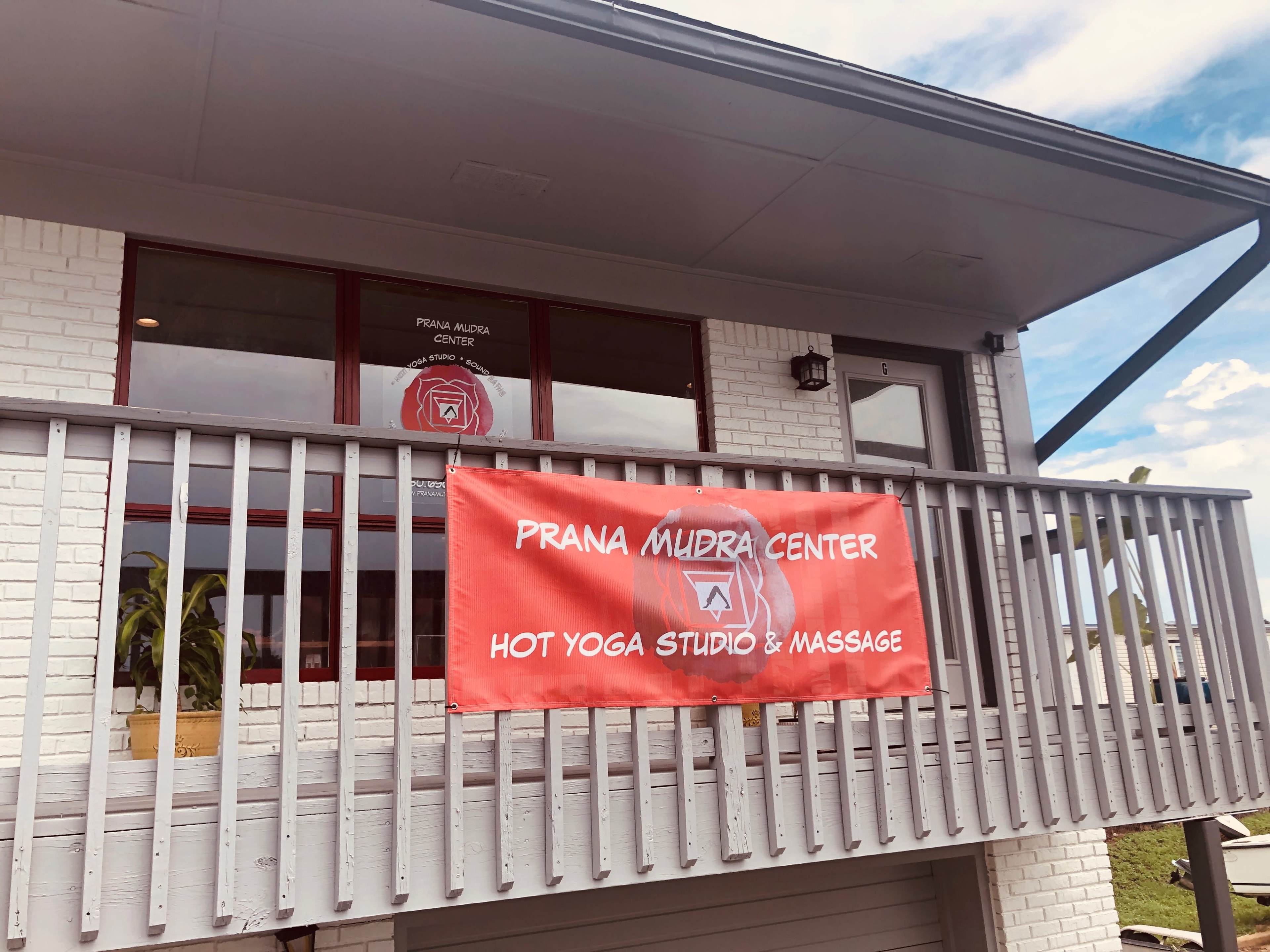 The image shows a building with a banner that reads "Prana Mudra Center Hot Yoga Studio & Massage" displayed on the railing of a balcony.