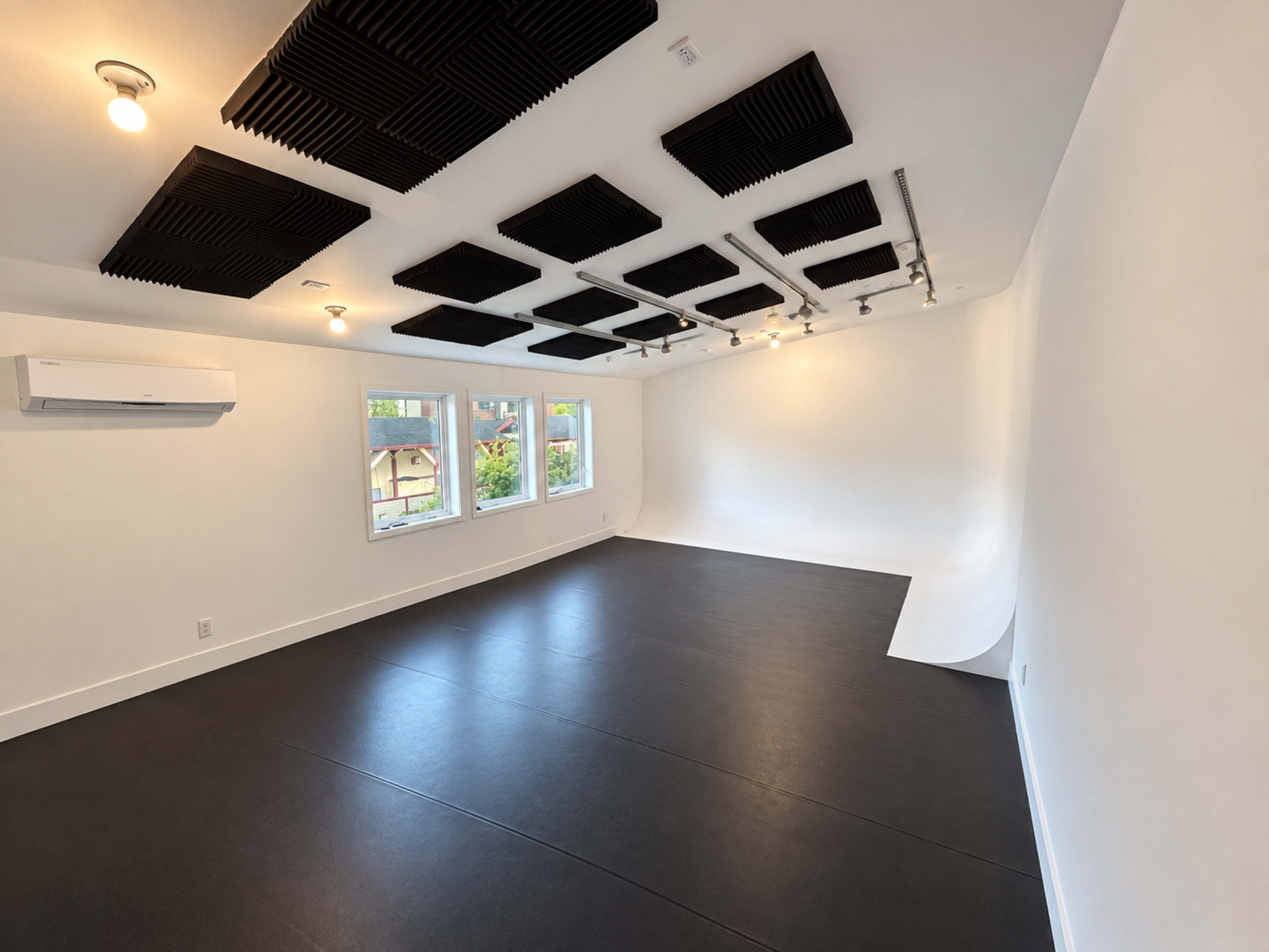 The image shows a spacious, well-lit room with black flooring, white walls, and soundproofing panels on the ceiling.