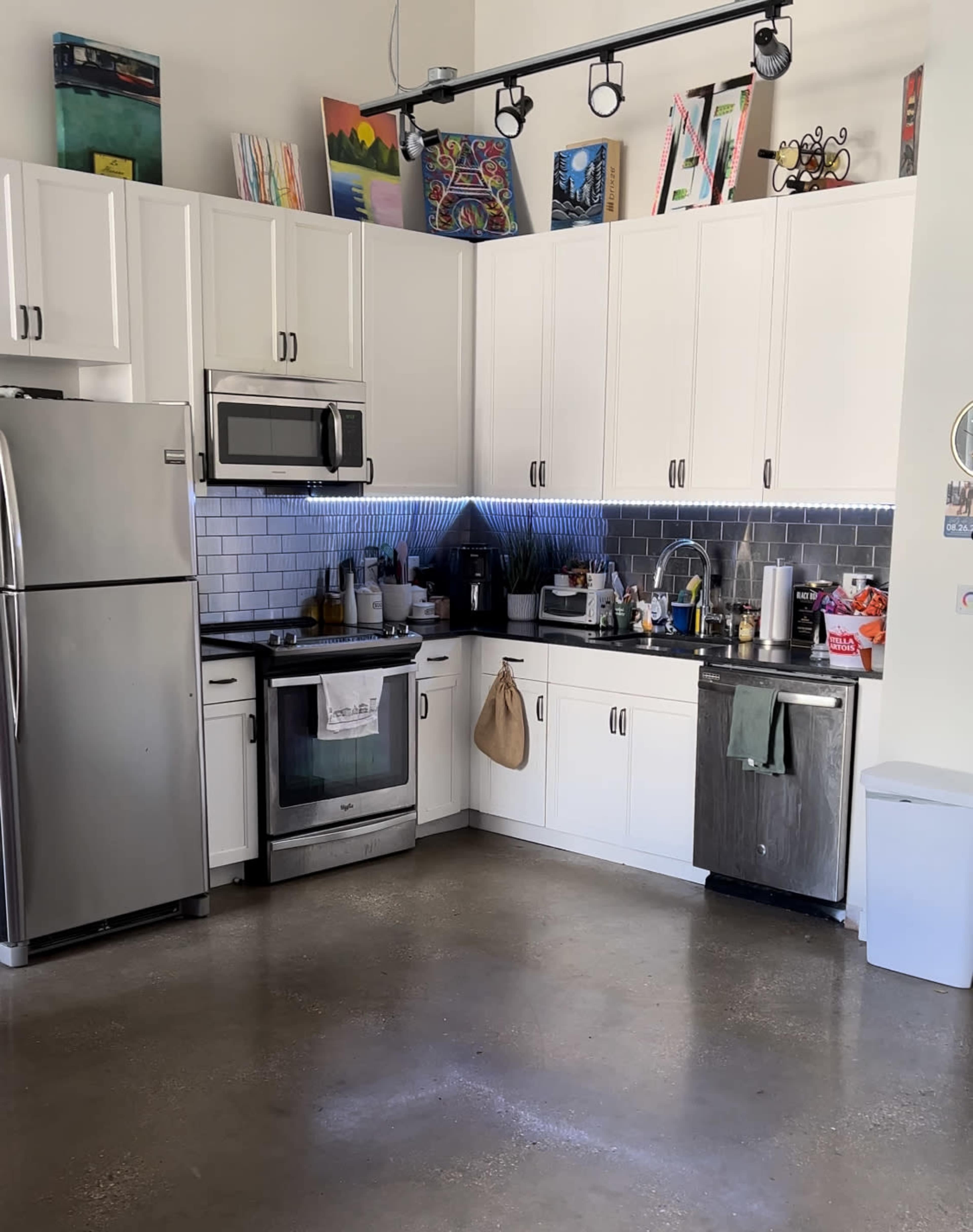 A modern kitchen with white cabinetry, stainless steel appliances, and a polished concrete floor.