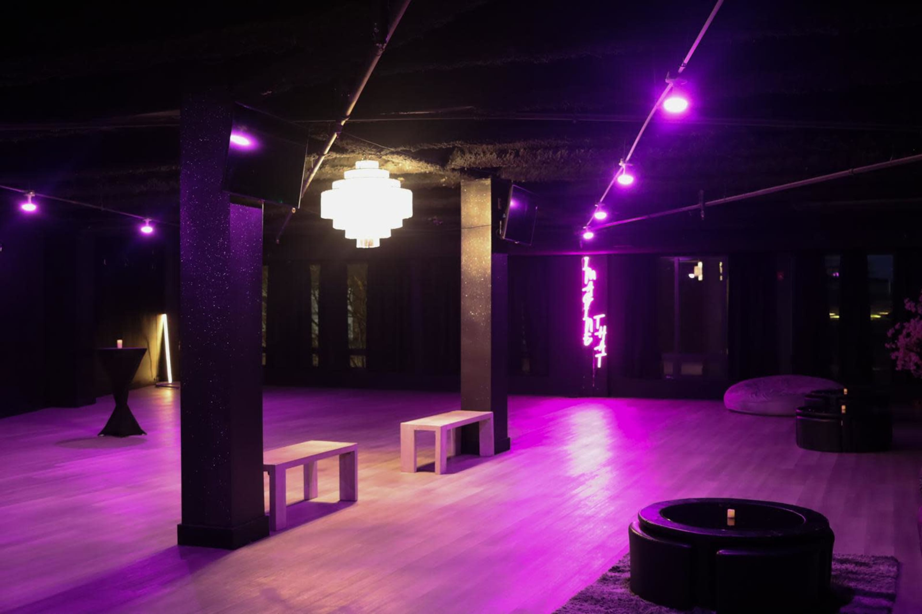 The image shows a dimly lit modern interior space with purple lighting, featuring minimalistic furniture and a large, decorative light fixture.