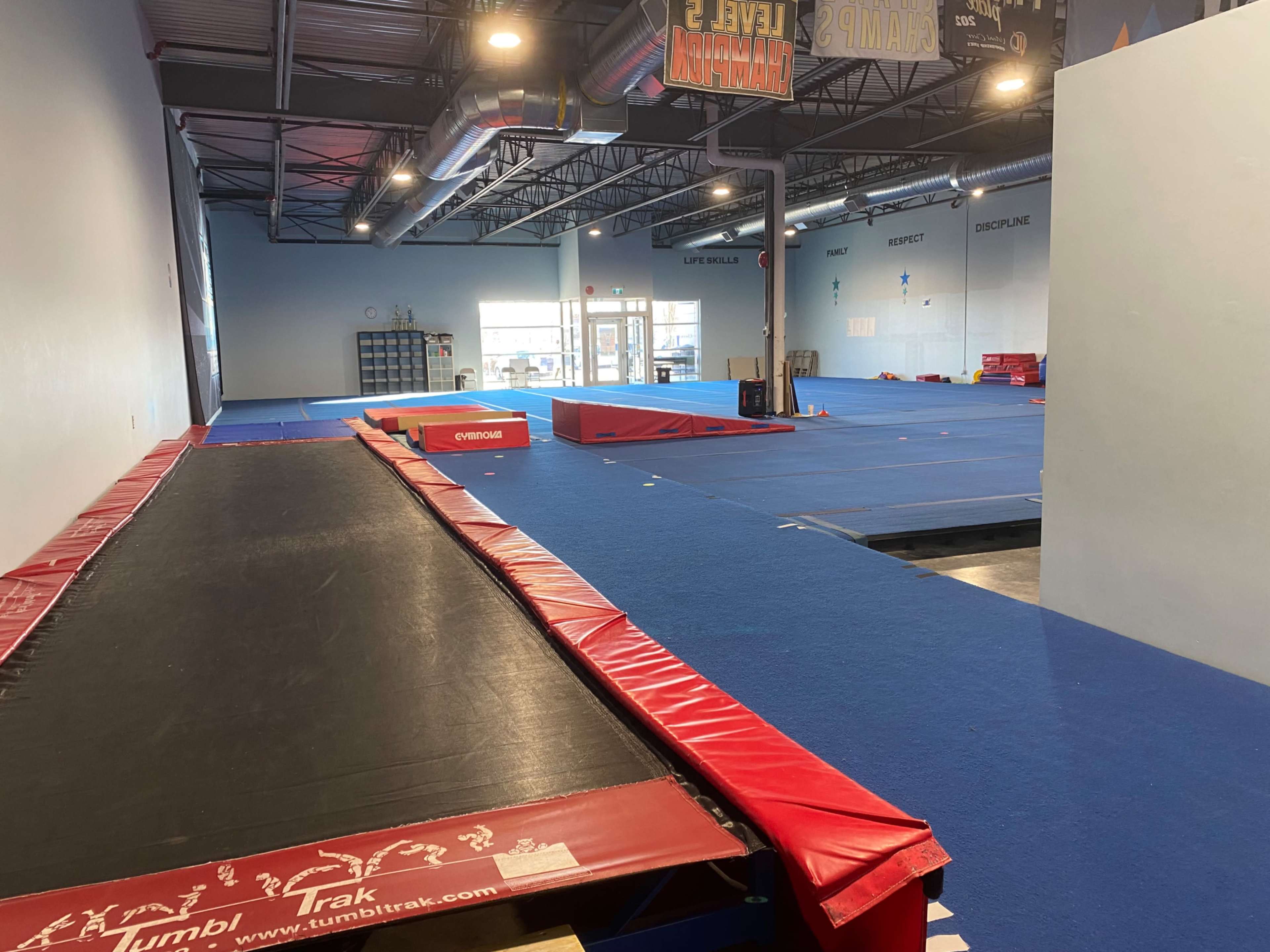 A gymnastics training facility with various mats and equipment arranged on a blue gym floor.