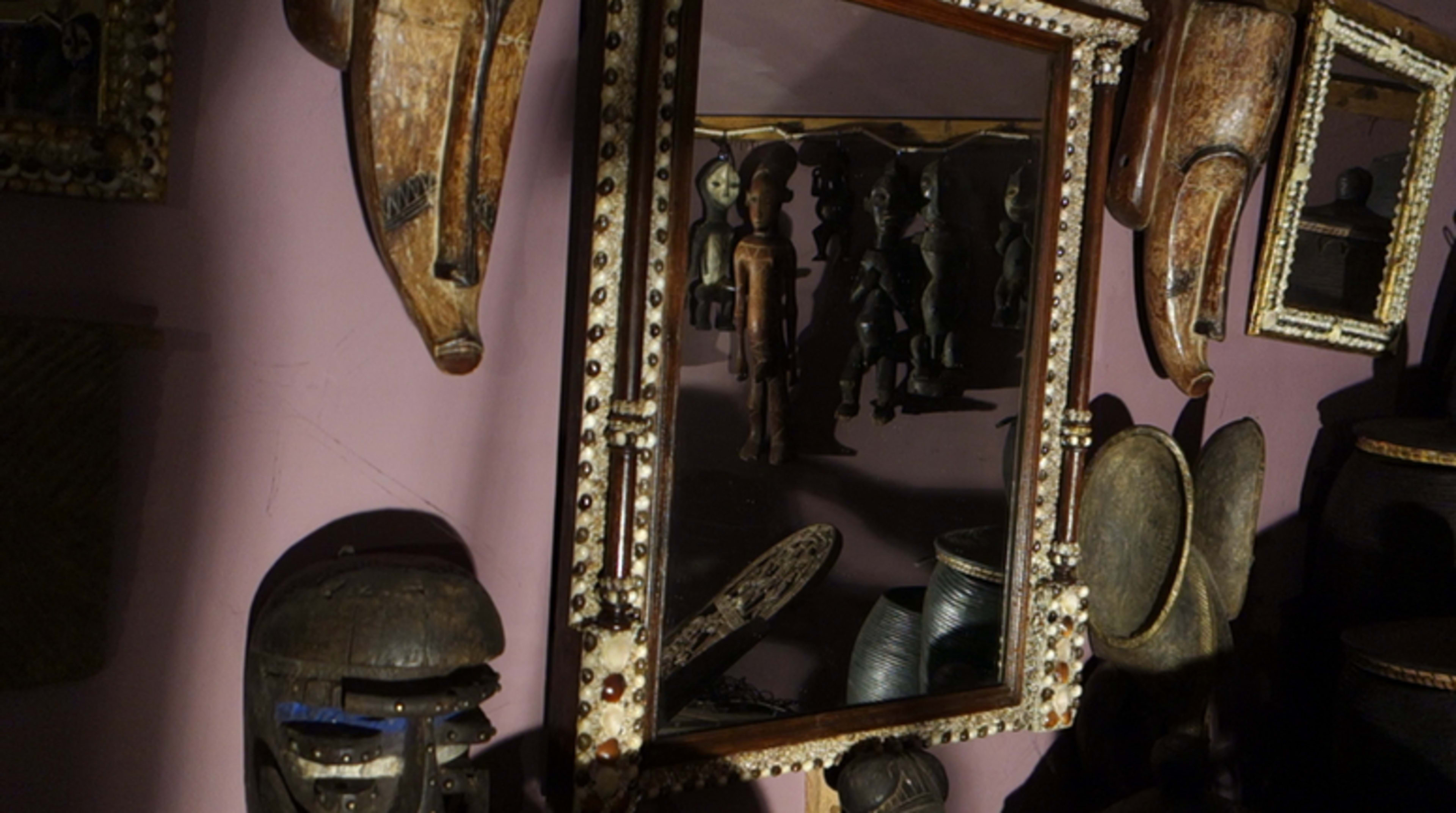 A collection of wooden masks and artifacts displayed on a wall, with a mirror reflecting other objects in the room.
