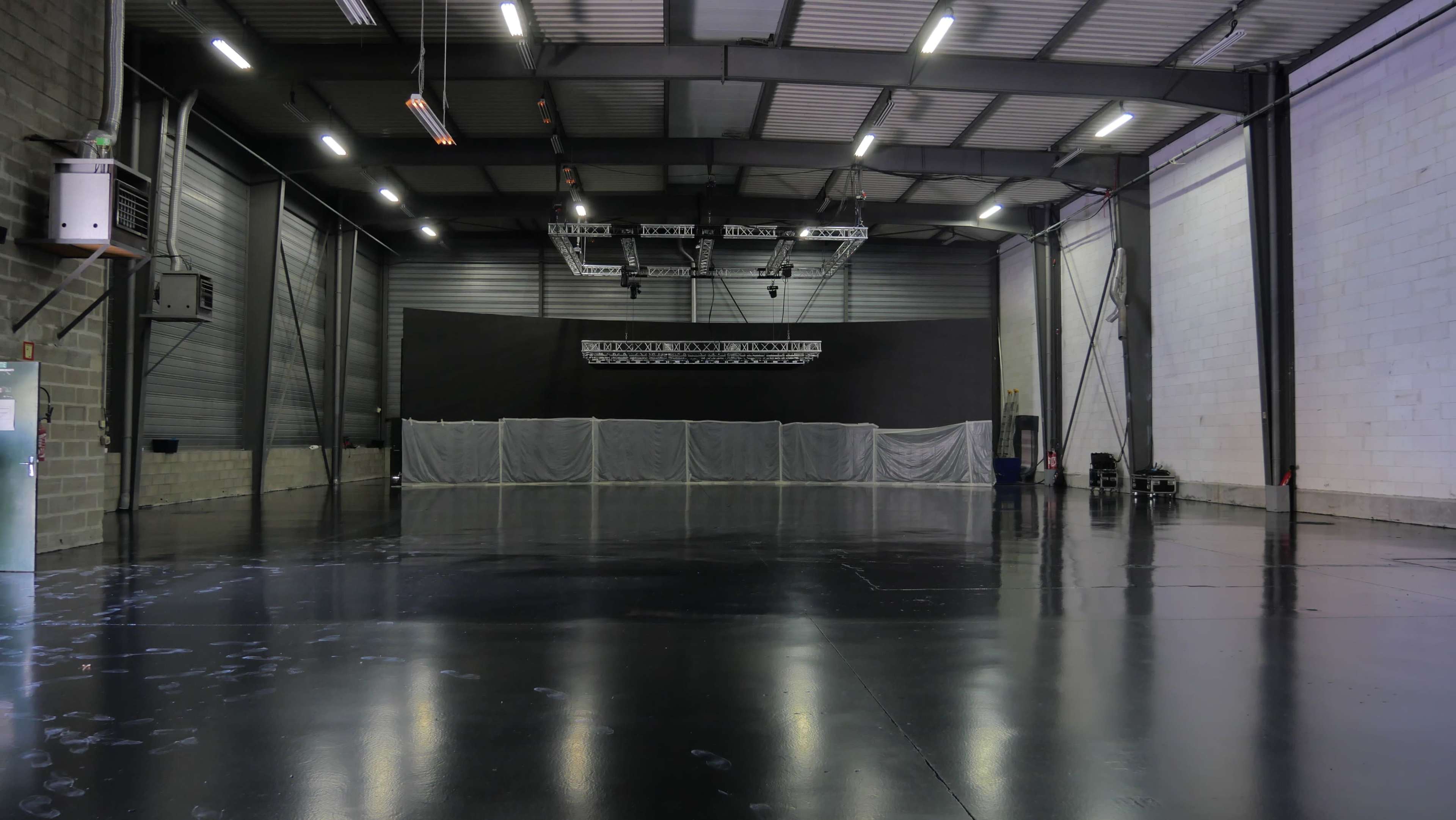 A large, empty event space features a shiny black floor, high ceilings, and a stage area covered with curtains at the far end.