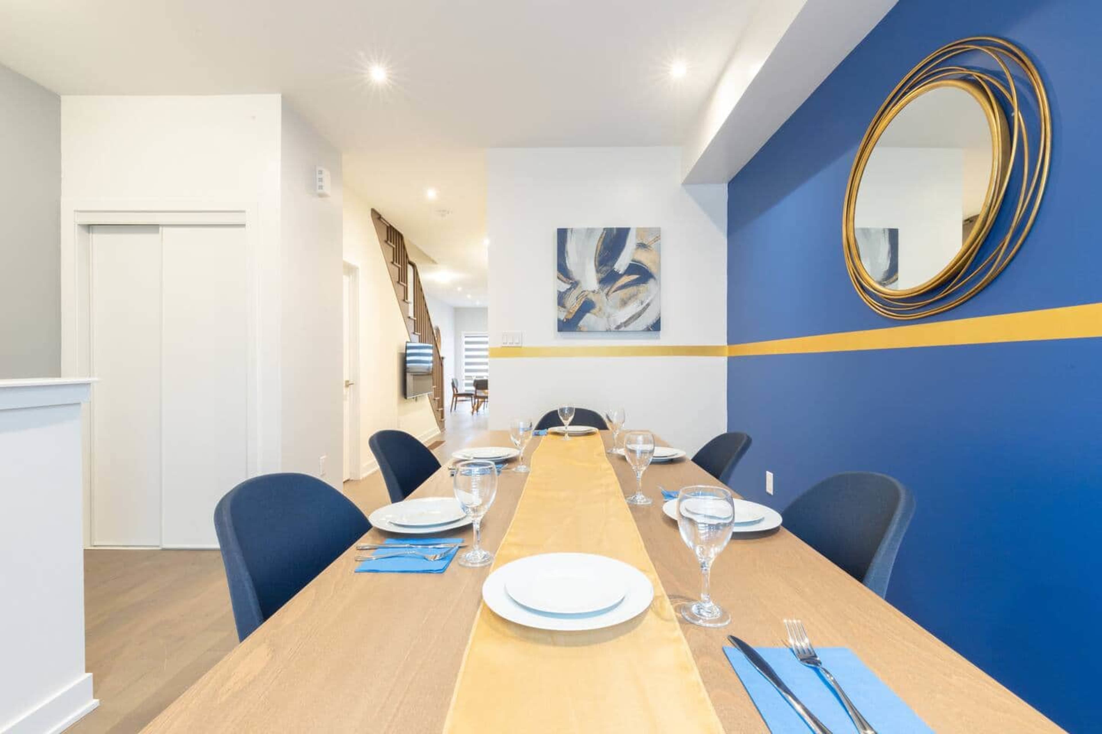 A dining table is set with plates and glasses in a well-lit room featuring a blue accent wall and a circular mirror.