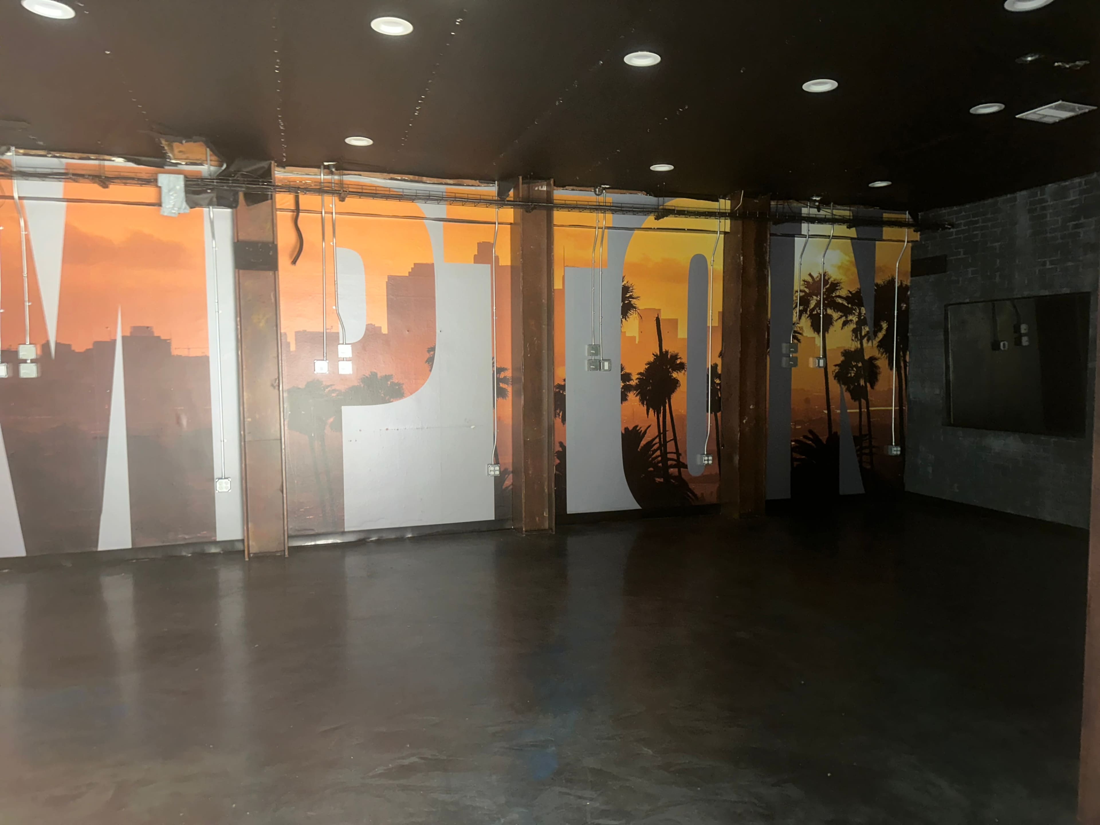 An empty room features a large mural with a sunset and palm trees on the walls.