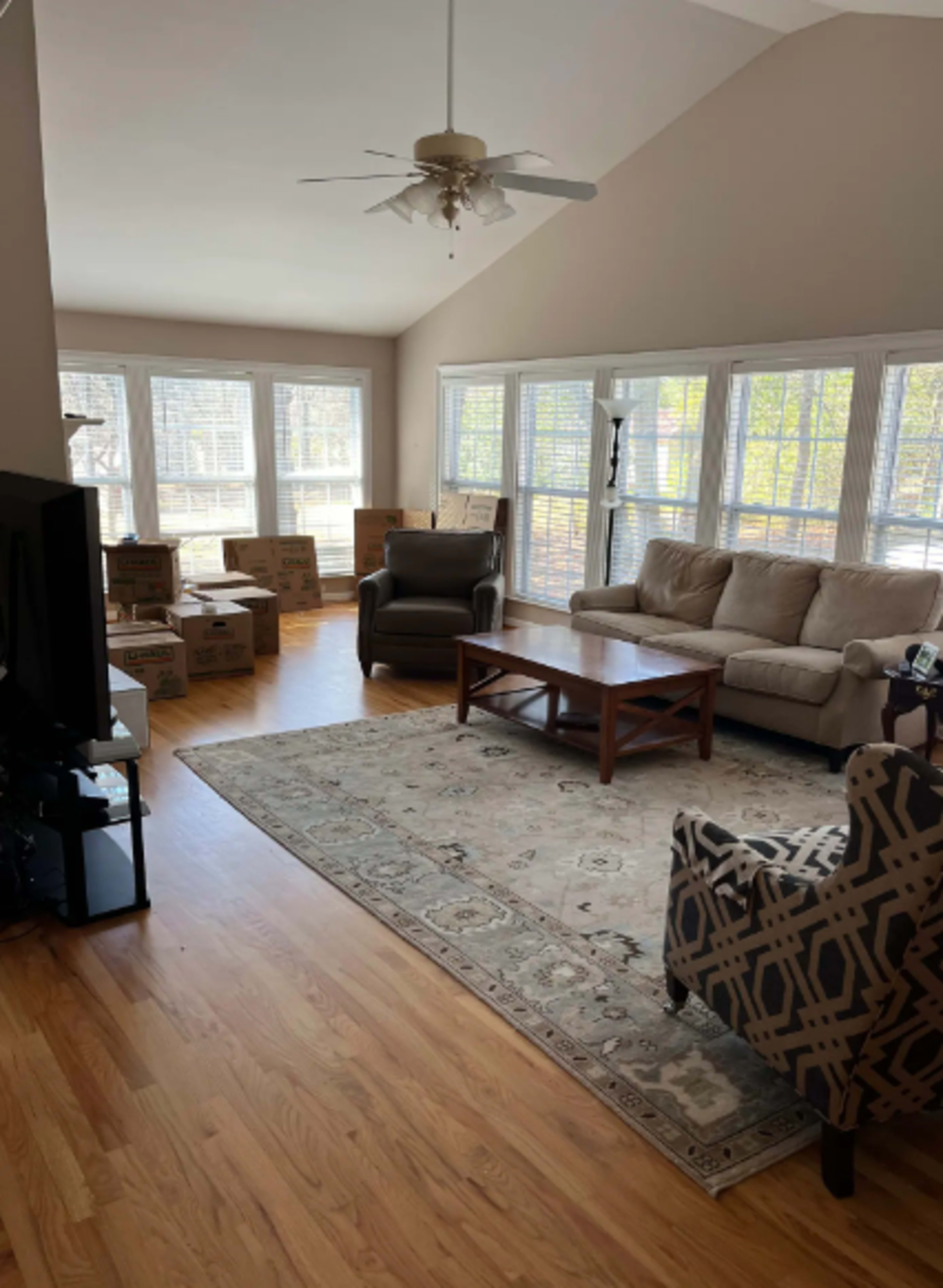 The living room features large windows, a sofa, two chairs, a coffee table, and several moving boxes stacked in the corner.