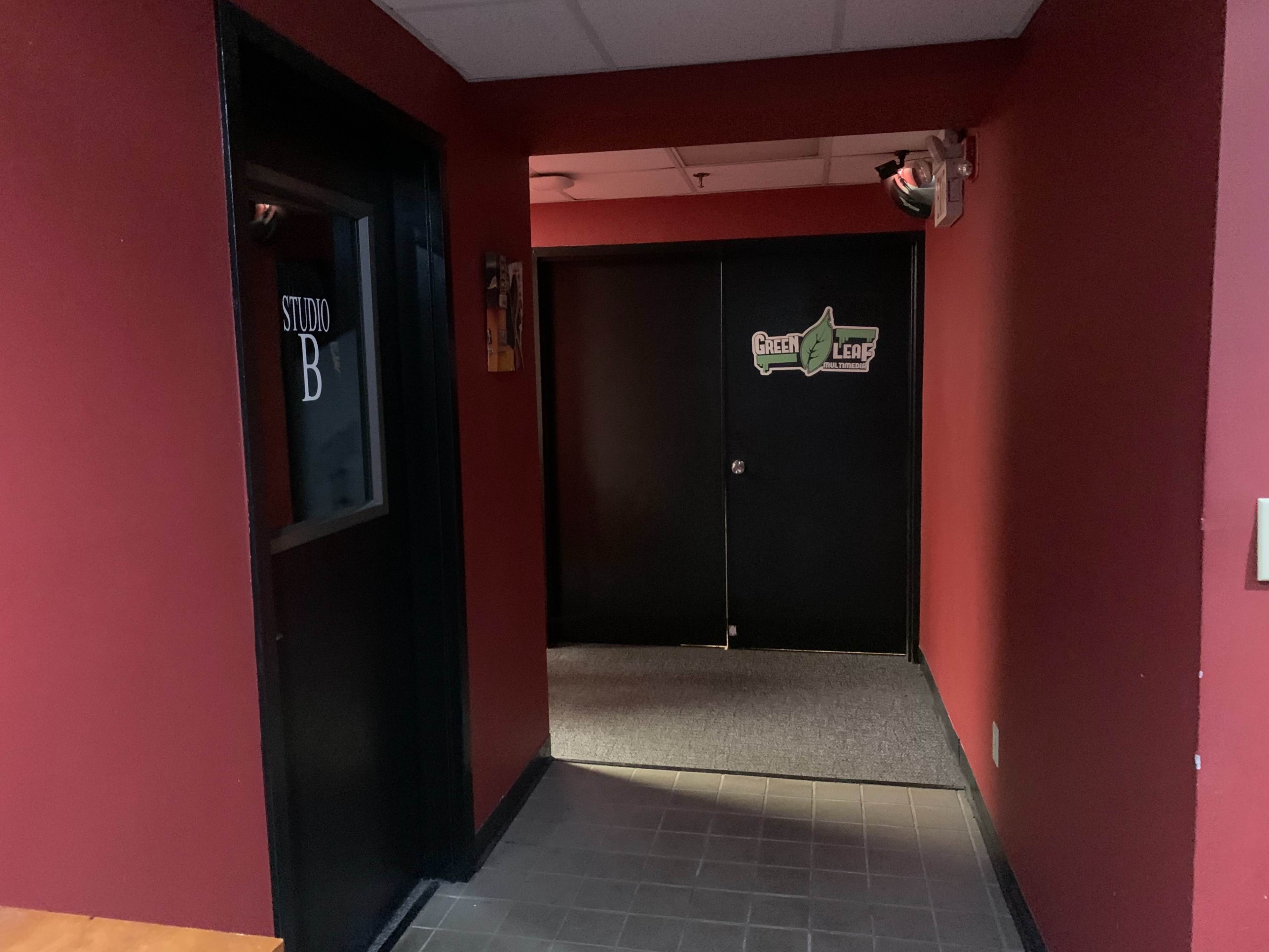 A narrow hallway with red walls, featuring a door labeled "STUDIO B" on the left and another door at the end with signage for "Green Lead."