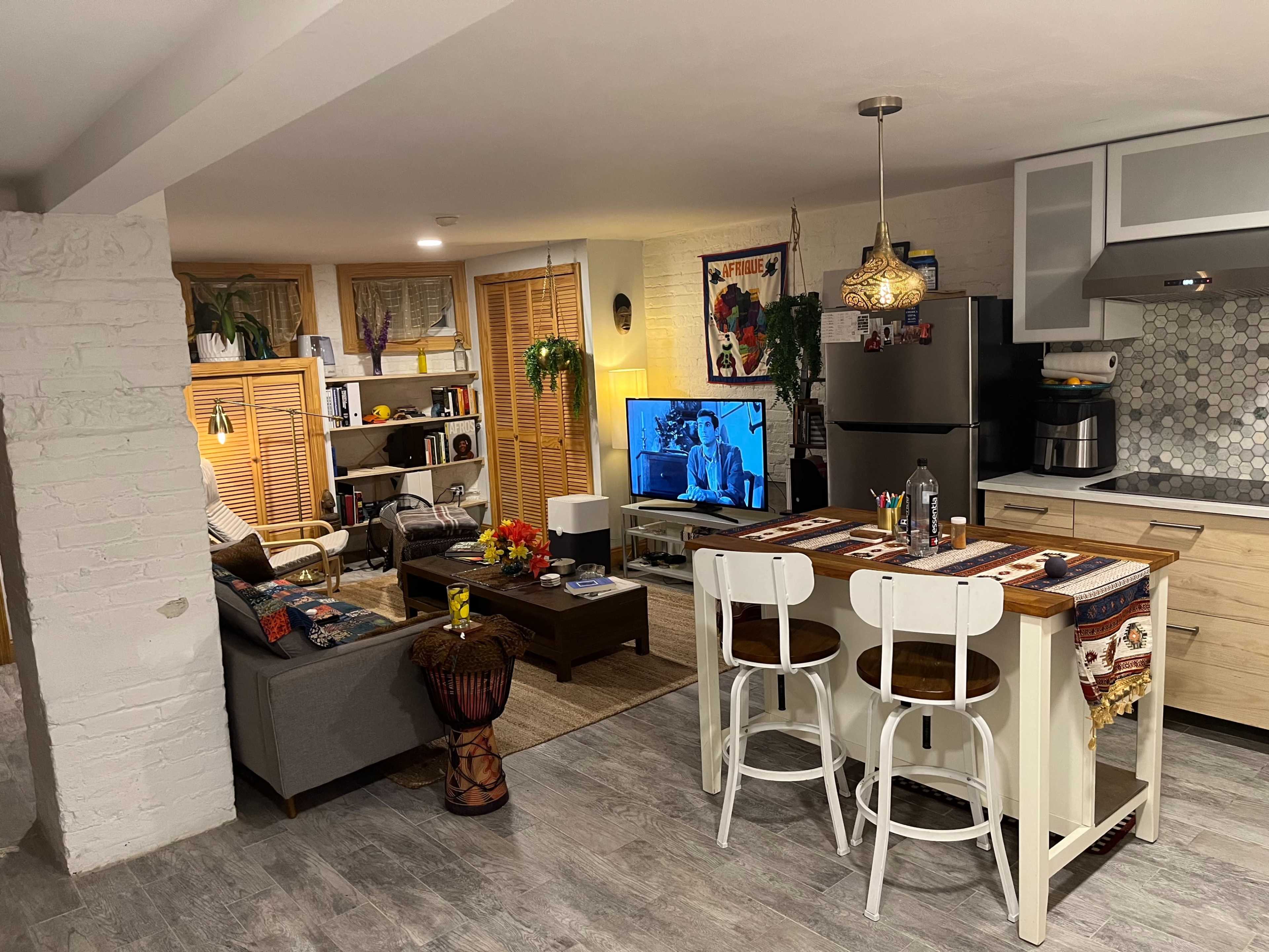 A modern kitchen and living area with a dining table, a sofa, a television, and decorative plants.