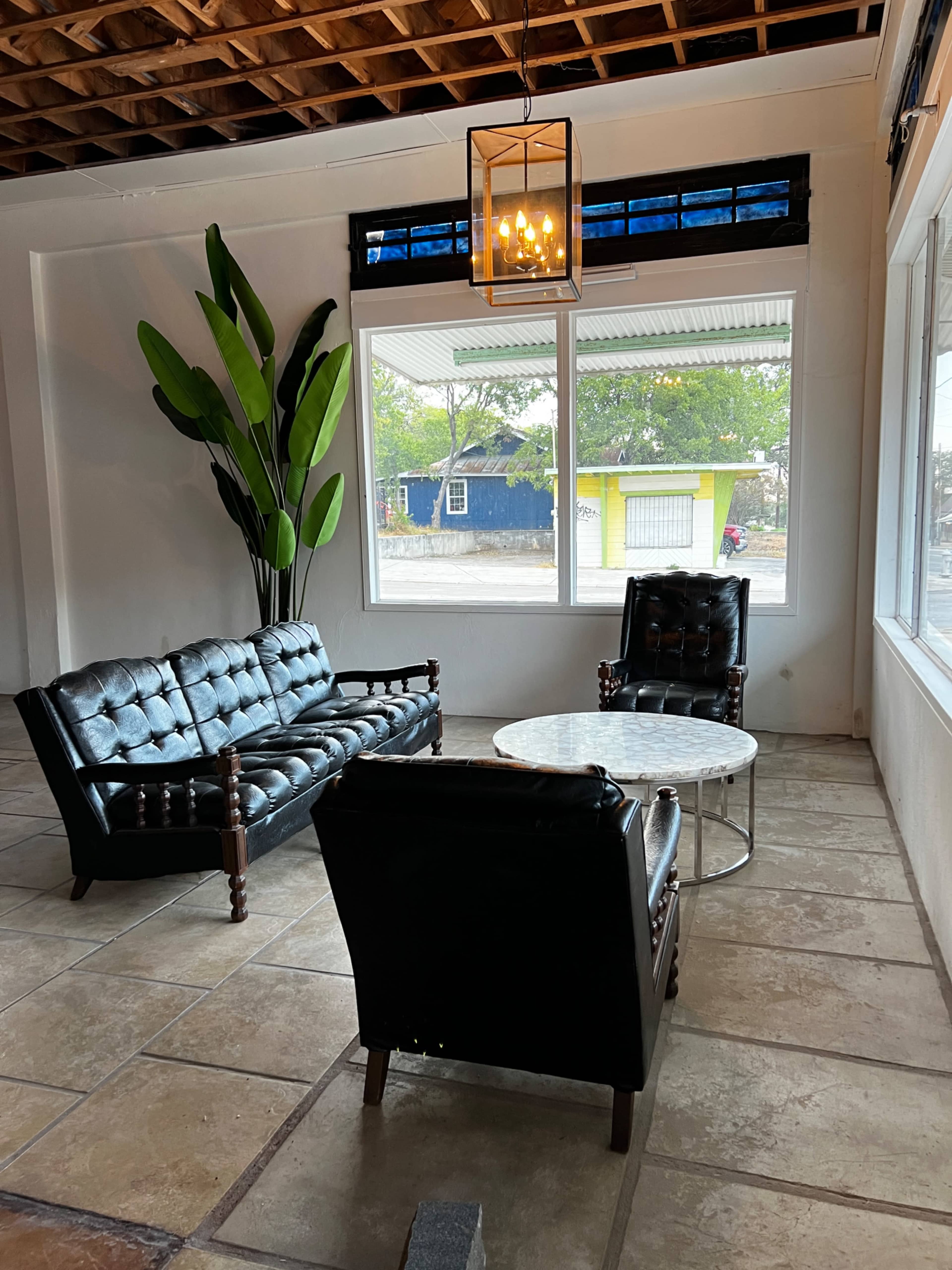 A seating area with a tufted black leather sofa, a pair of matching armchairs, a round marble coffee table, and a large potted plant next to a window.