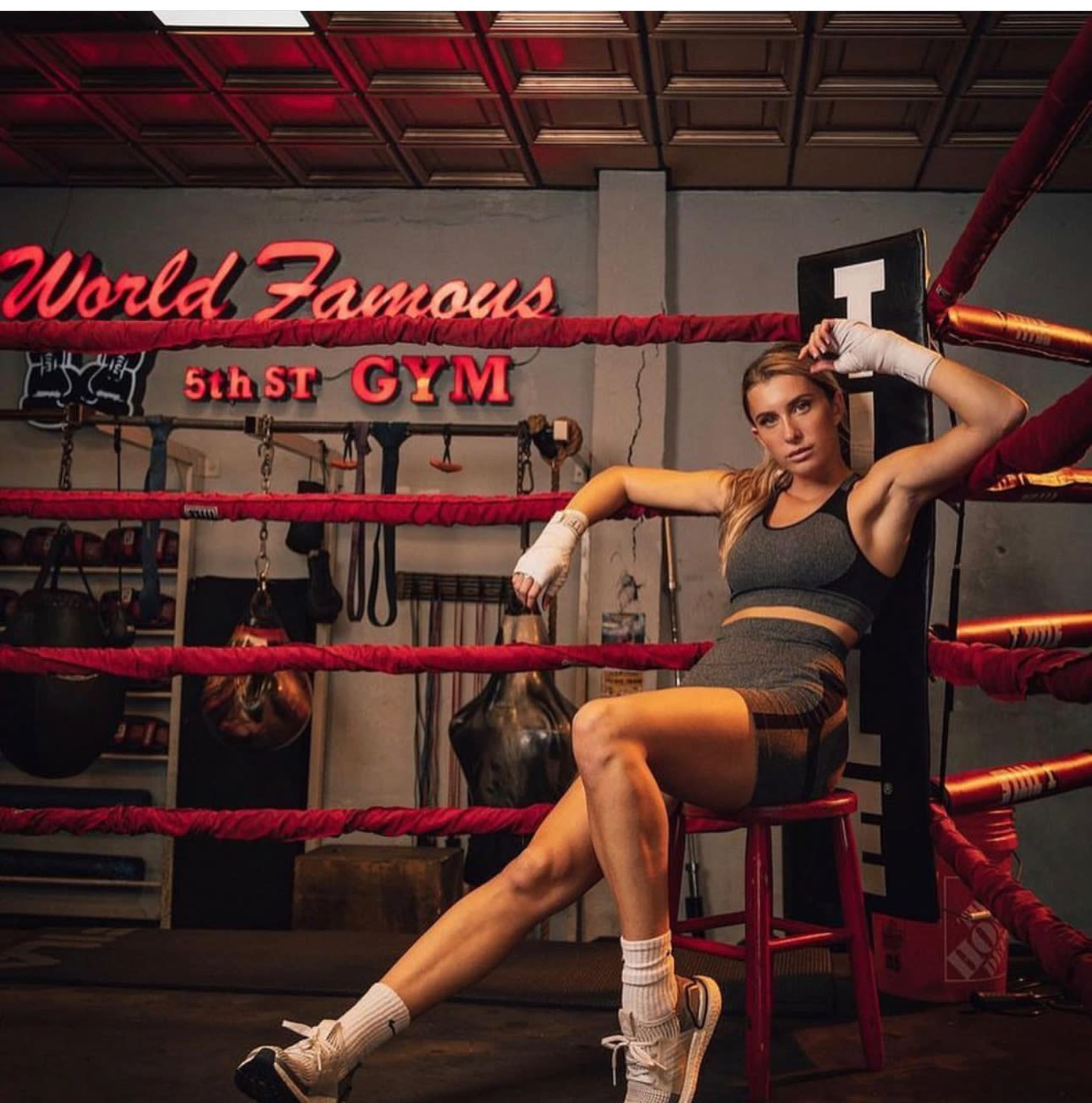 A boxer sits on a stool in a gym, surrounded by red boxing ropes and a sign that reads "World Famous 5th St GYM."