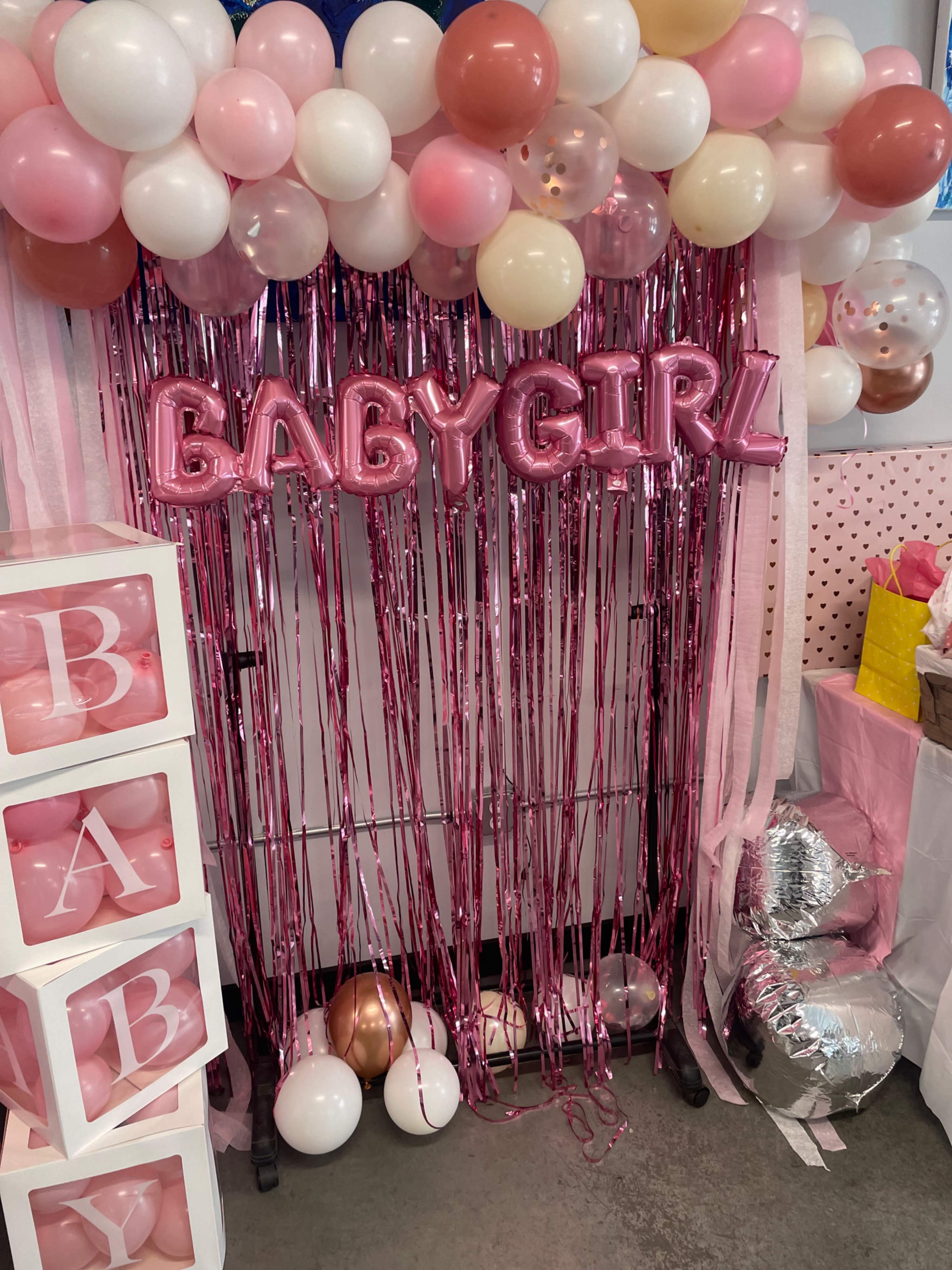 The scene features a decorative setup with pink and pastel balloons, a "BABY GIRL" balloon banner, and shimmering fringe curtains.