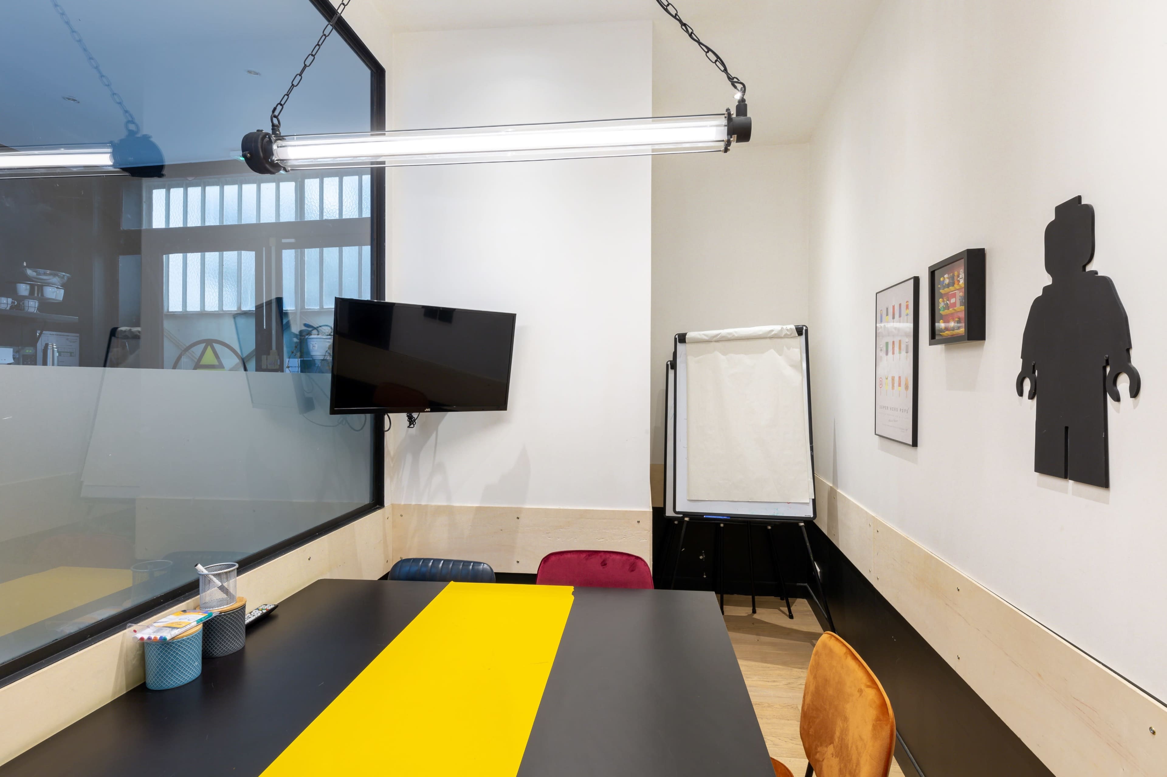 A conference room features a black table with a yellow stripe, a television mounted on the wall, and an easel for presentations.