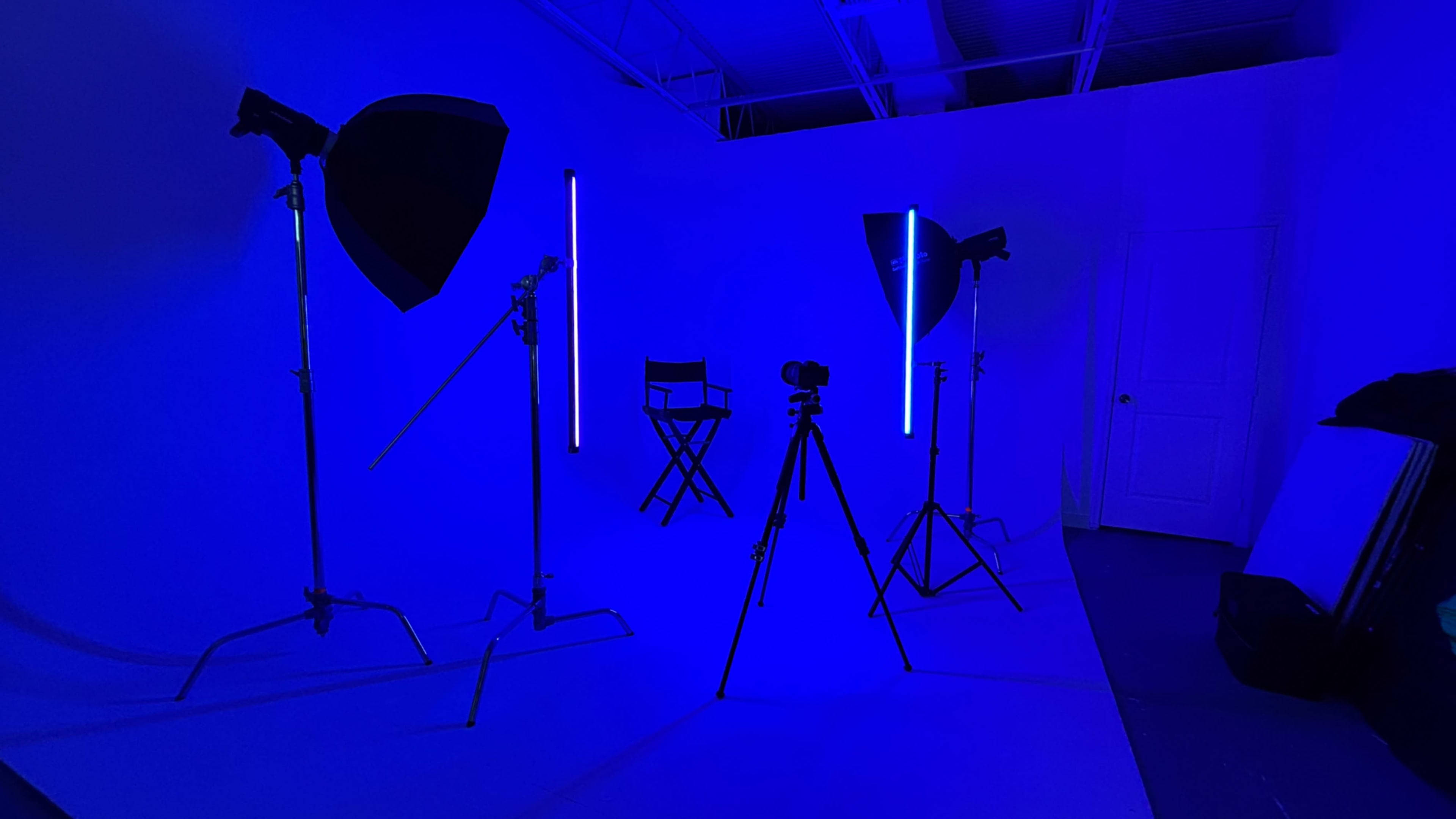 A photography studio features blue lighting with various lighting equipment and a director's chair.