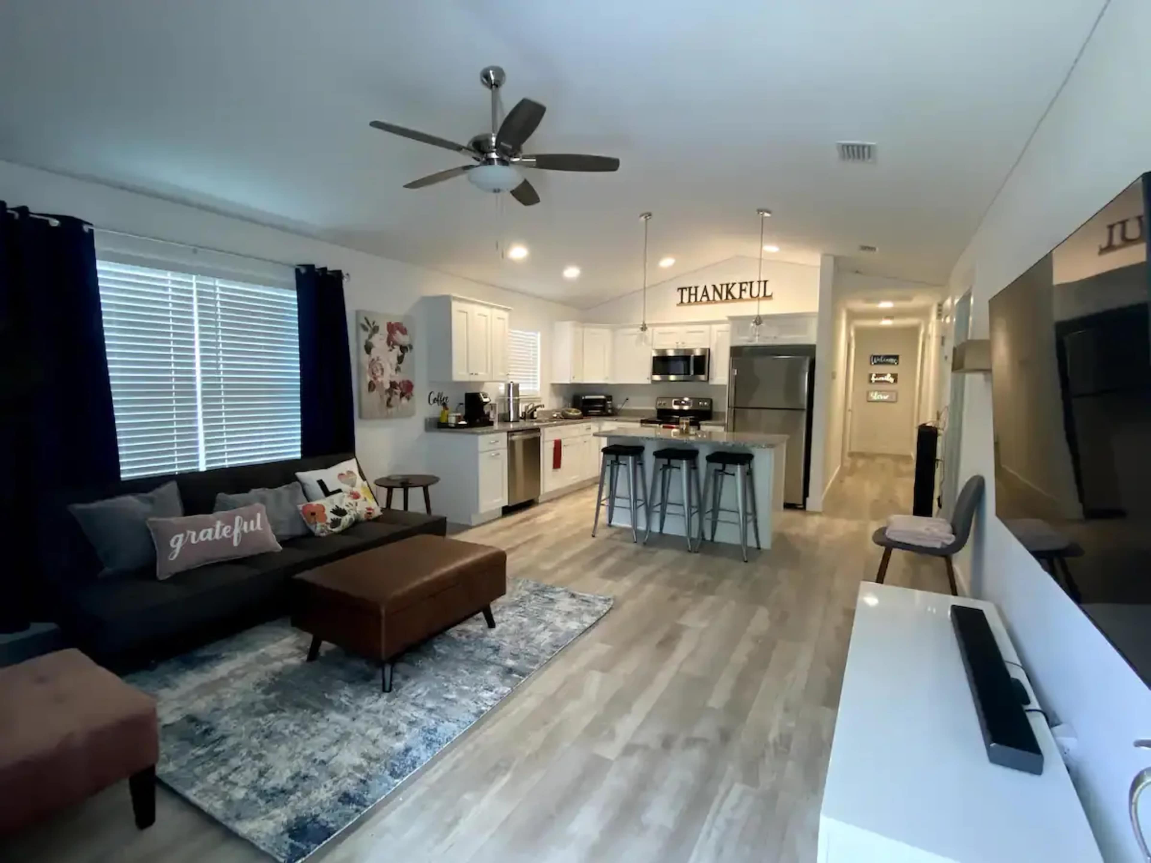 A modern living room and kitchen area featuring a gray sofa, a coffee table, and a dining island with bar stools.