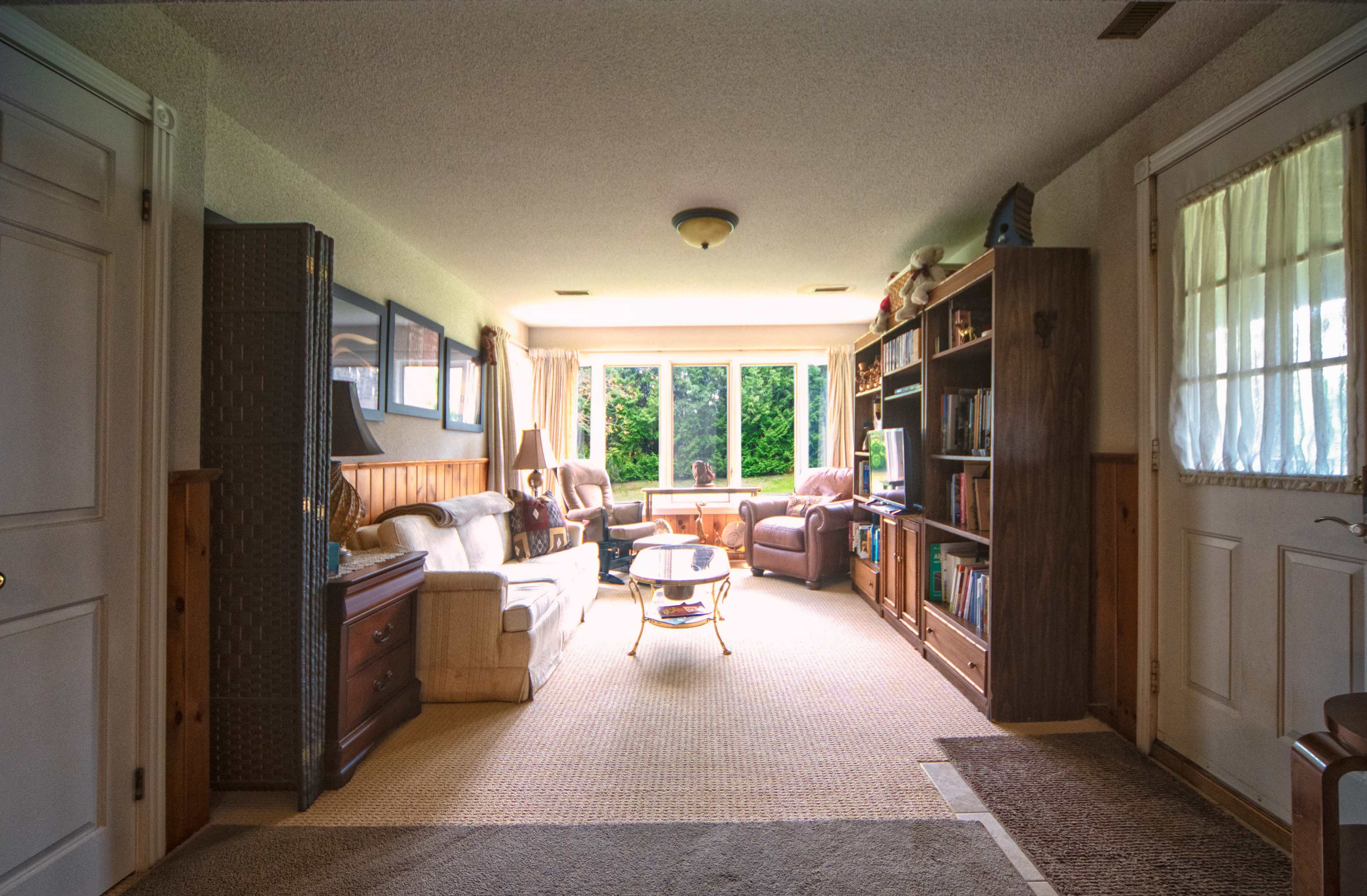 A long hallway leads to a sitting area with large windows, furnished with a sofa, two chairs, a coffee table, and bookshelves along the walls.