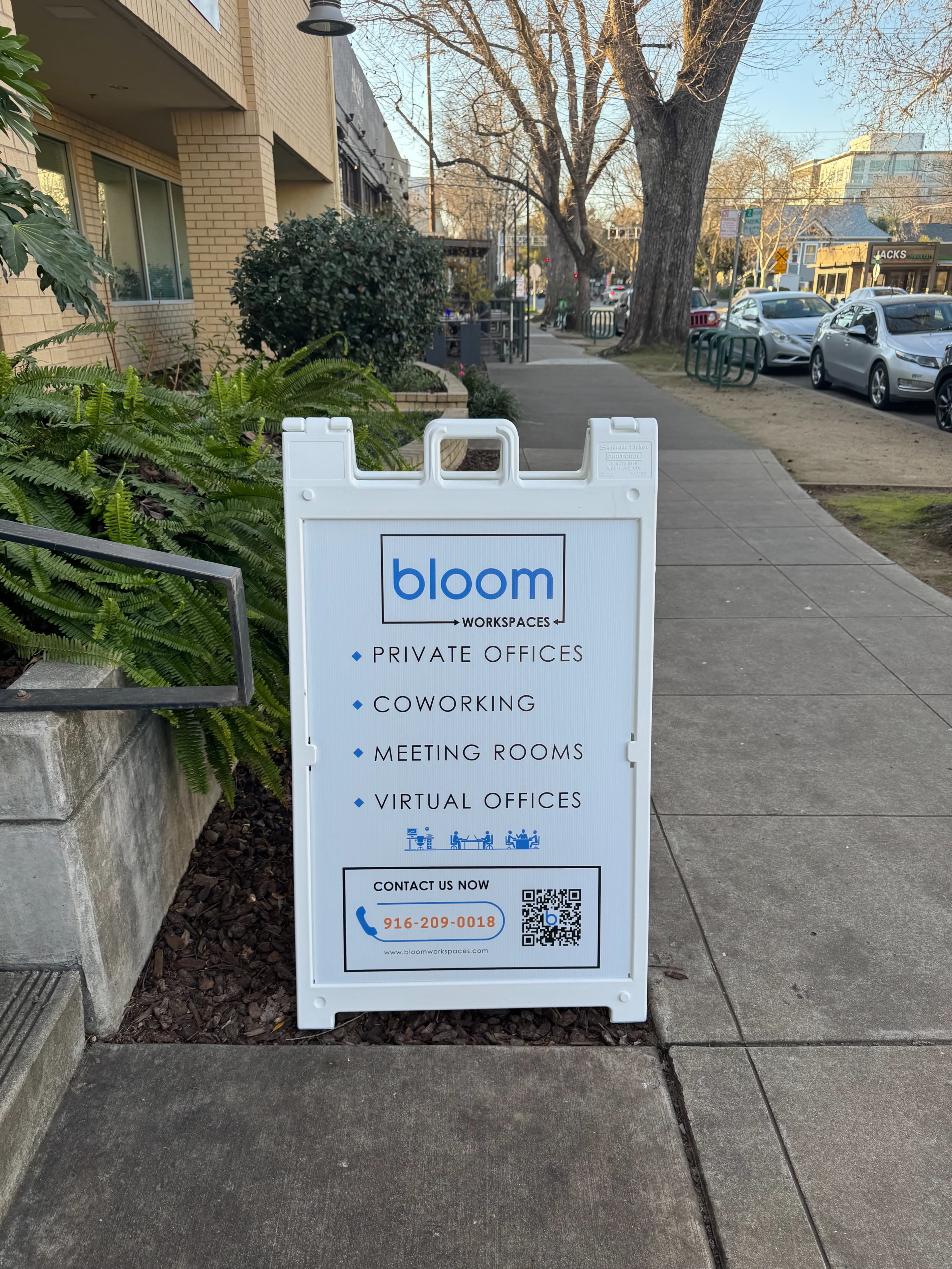 A sidewalk sign for a business called "bloom" displays information about private offices, coworking spaces, meeting rooms, and virtual offices.