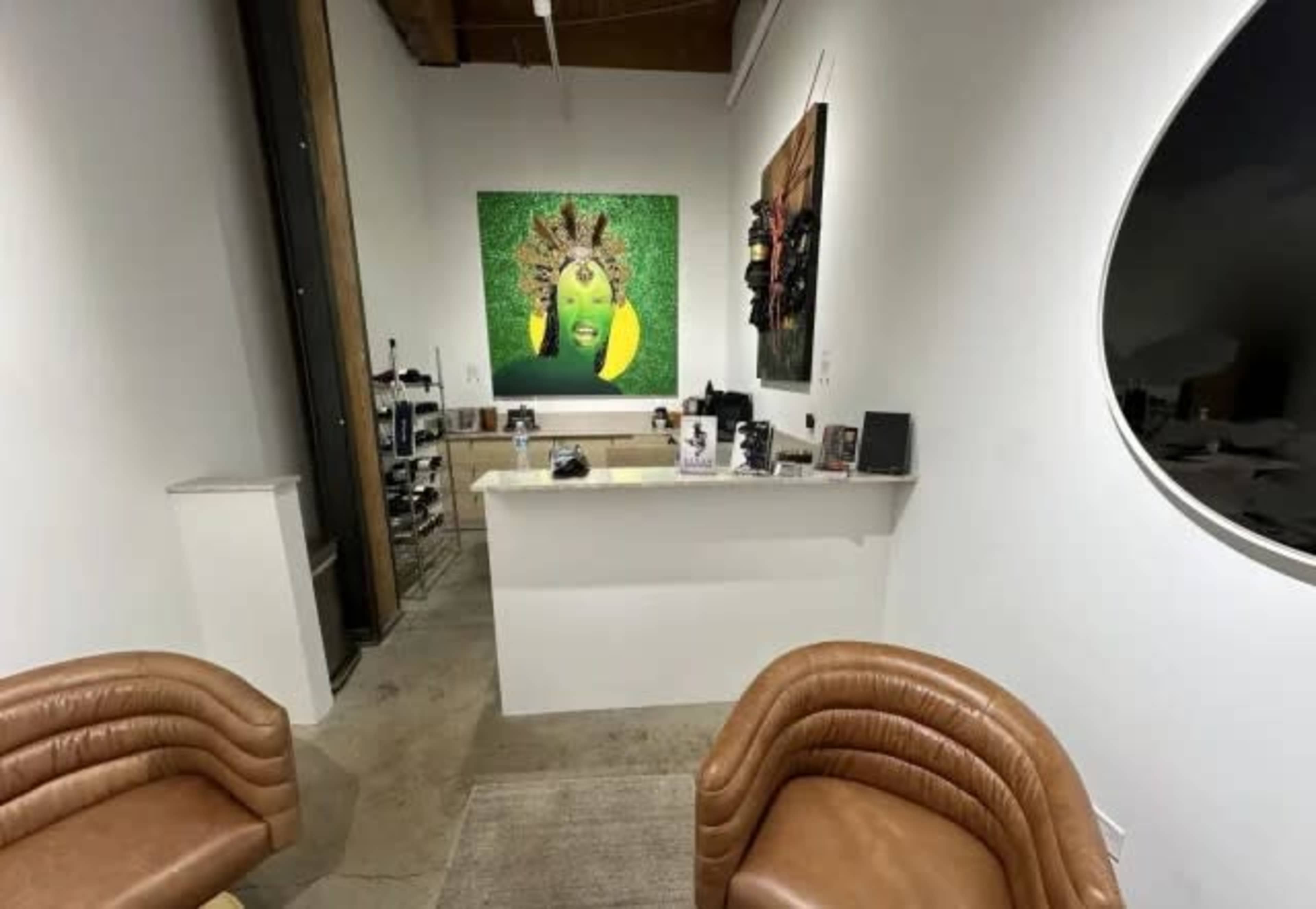 The image shows a modern interior space featuring two brown upholstered chairs, a countertop with various items, and a large green artwork on the wall.