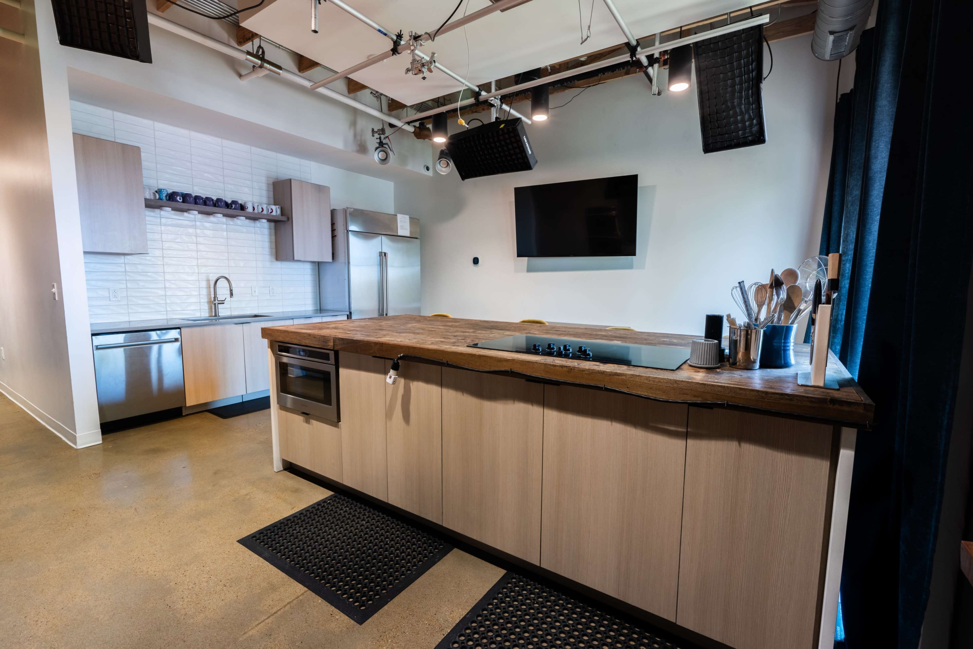The image shows a modern kitchen with a large wooden island, stainless steel appliances, and minimalist cabinetry.