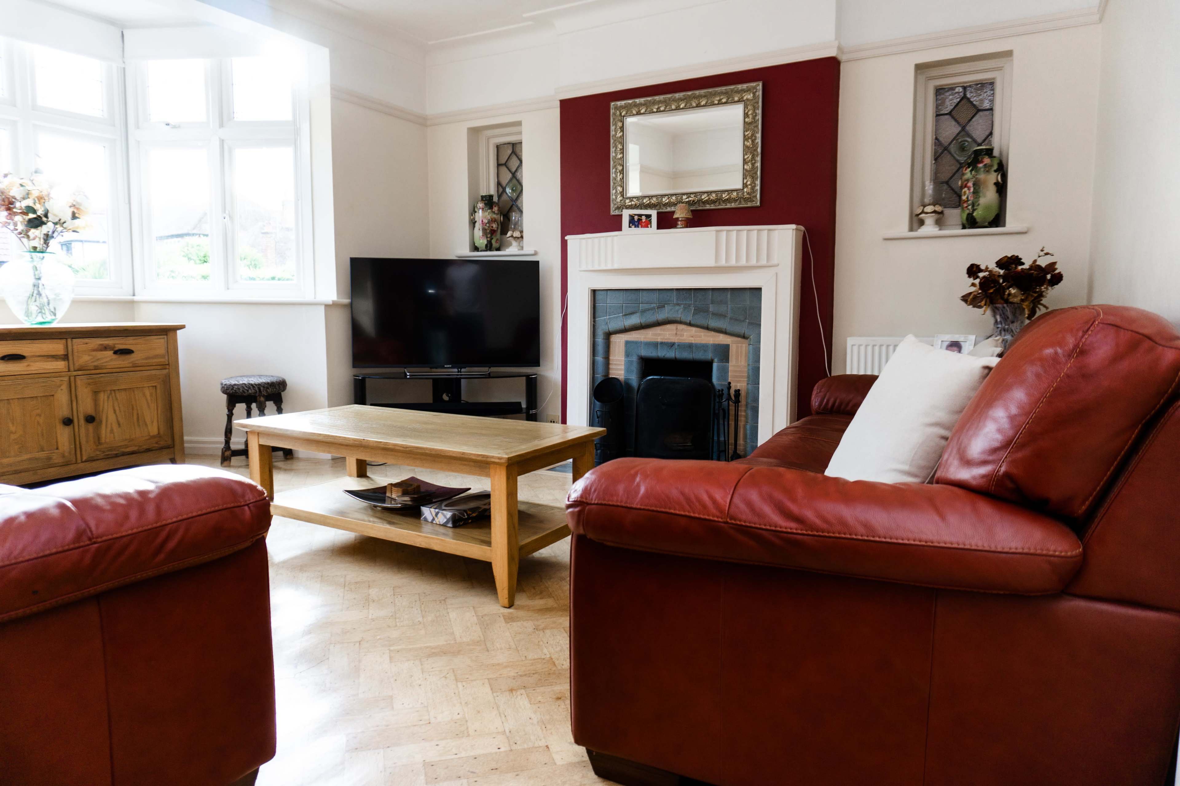 A cozy living room features two red leather sofas facing a wooden coffee table, a television, and a fireplace with decorative elements.