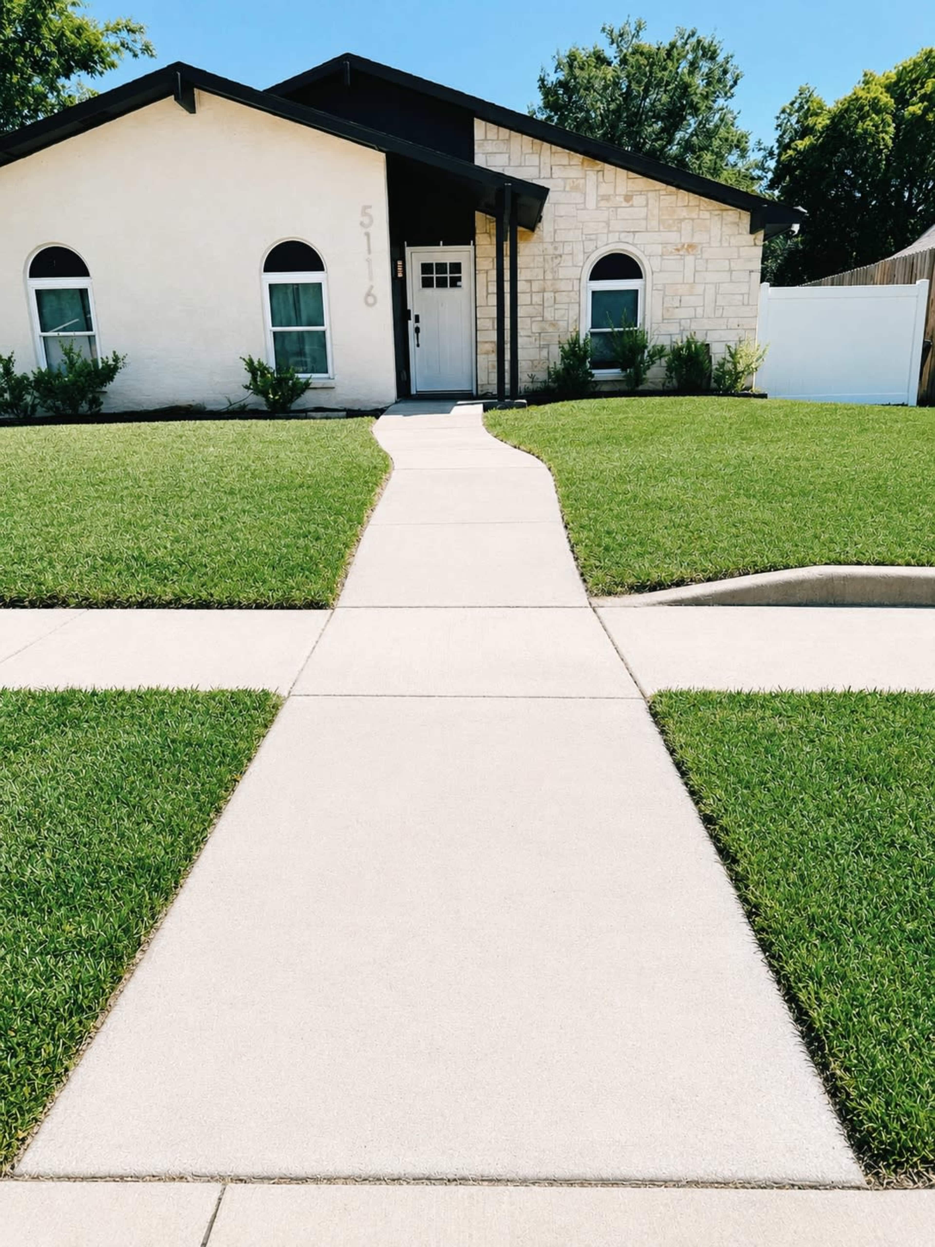 The image shows a house with a stone and stucco exterior, a small walkway leading to the front door, and well-maintained grass on either side.
