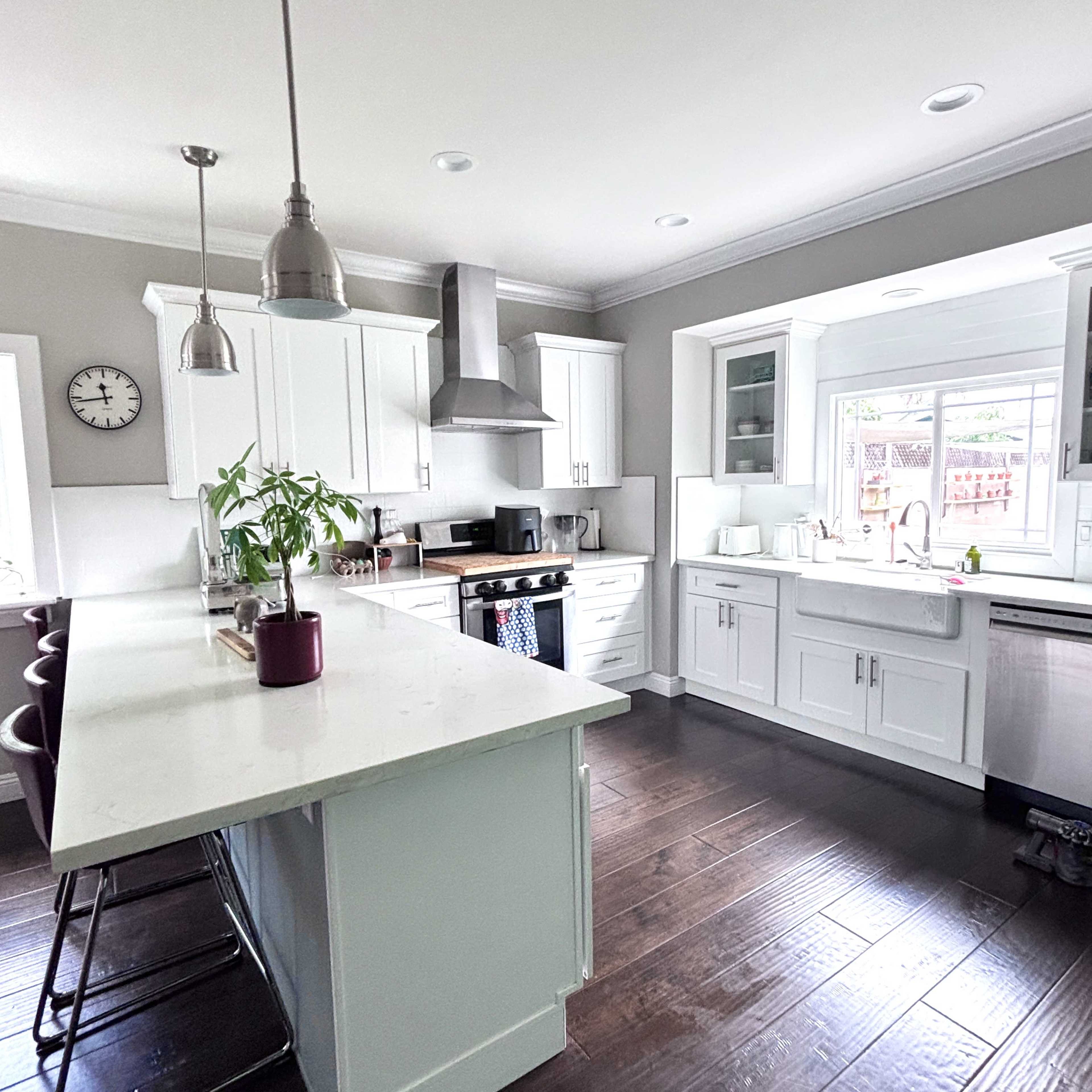 A modern kitchen features white cabinets, stainless steel appliances, a large island, and hardwood flooring.